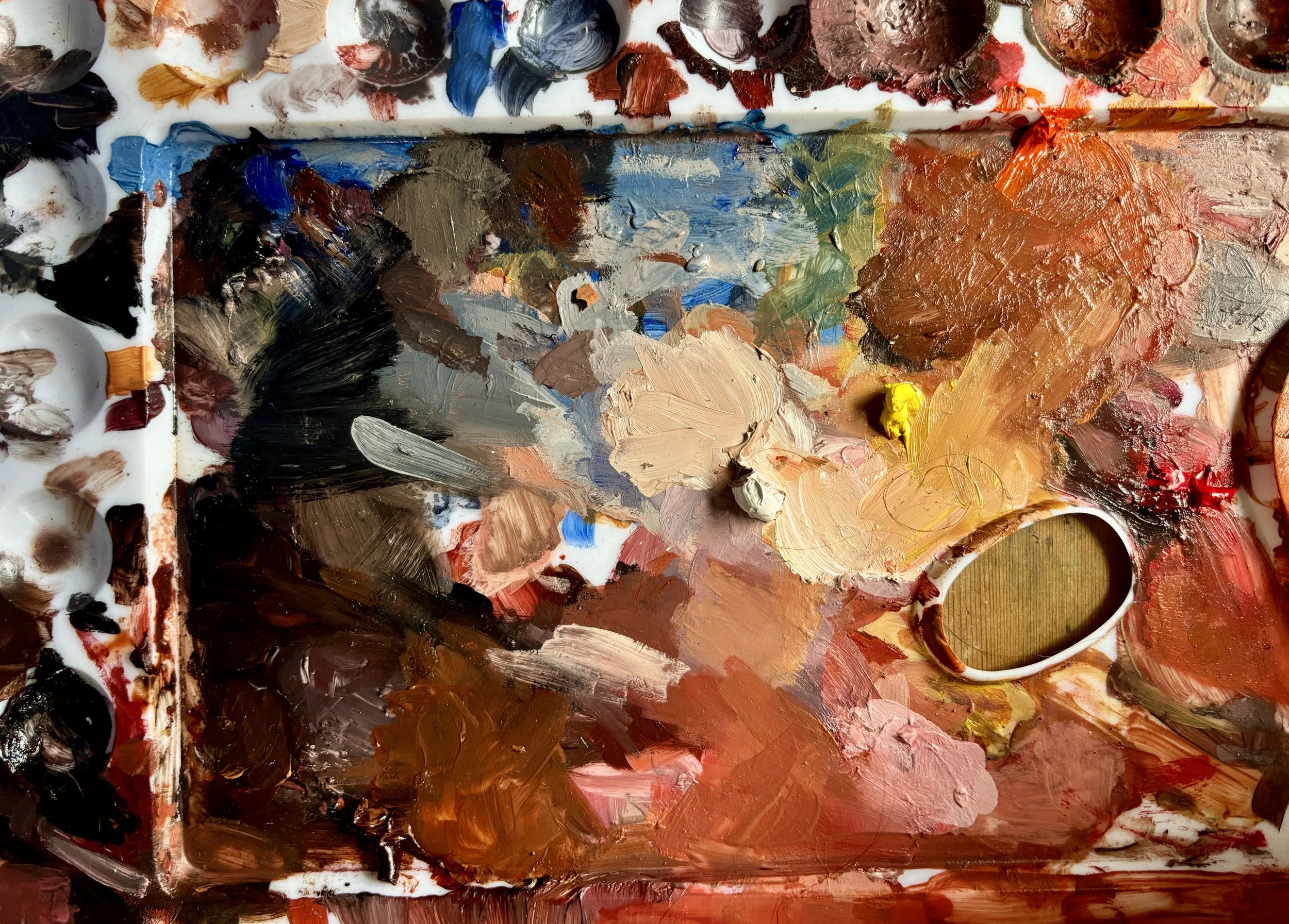 A colorful artist's palette with various blobs and mixes of Oil paints in black, blue, brown, green, yellow, red, and earth tones.