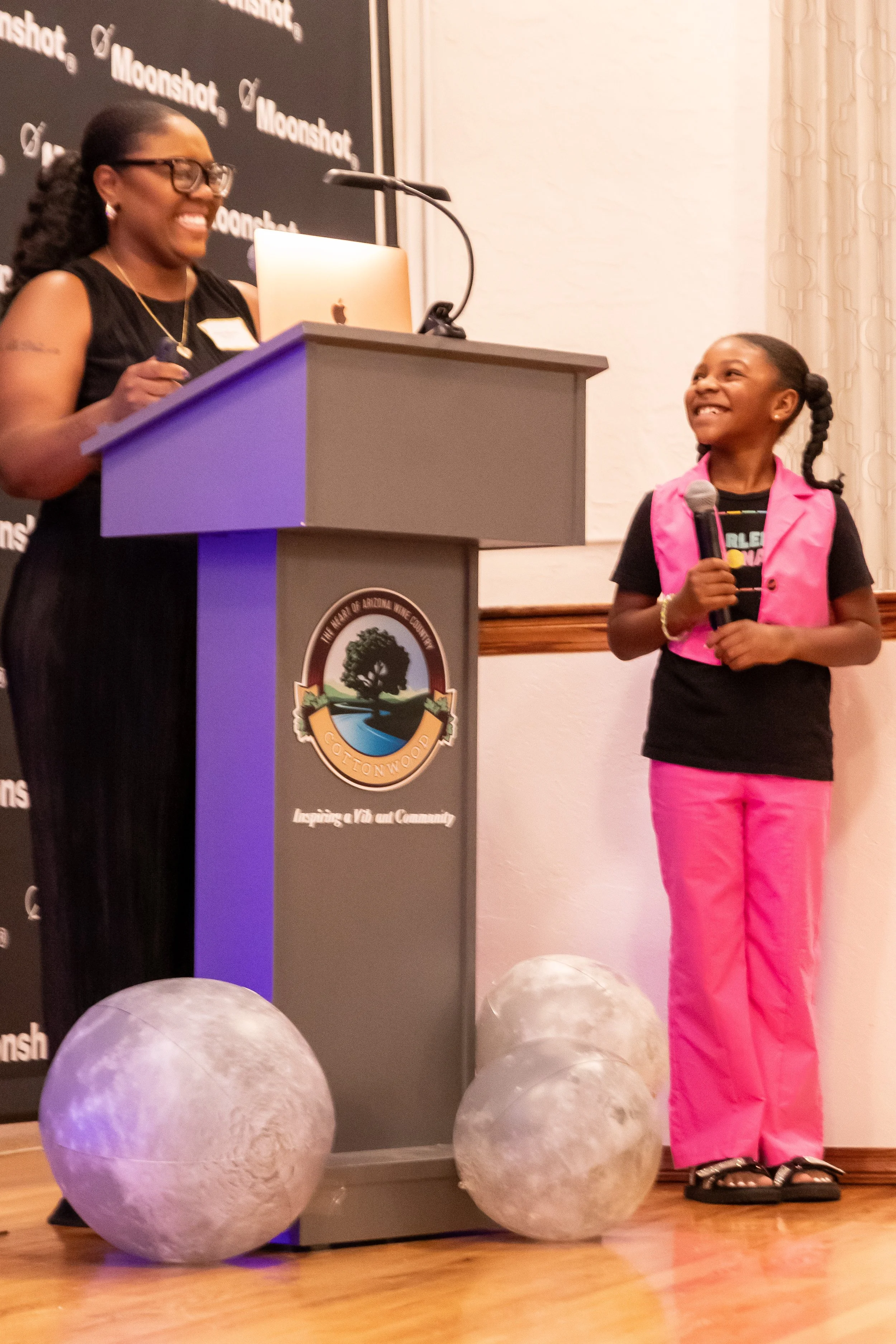 A woman and a girl standing at a podium with a Michigan Tech logo, holding microphones and smiling, during an event.