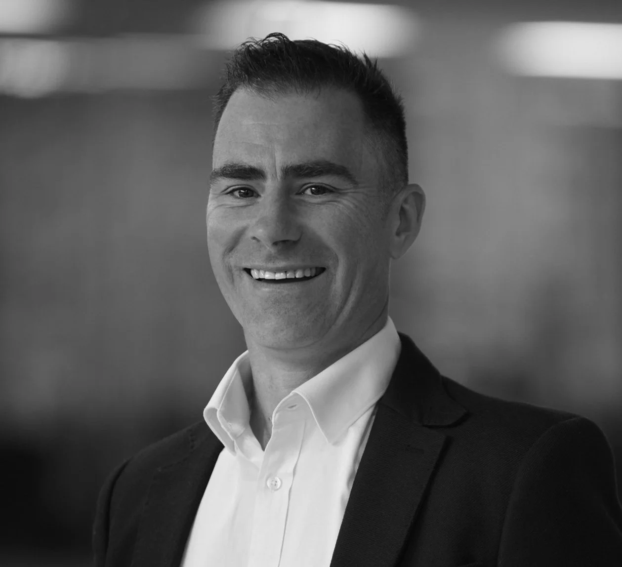 Black and white headshot of a smiling man in a suit and white shirt.