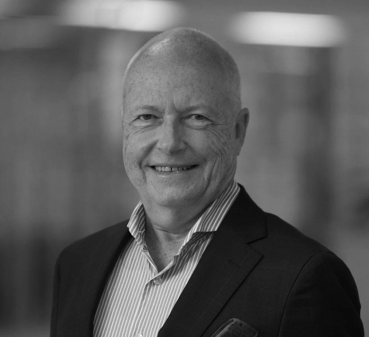 Black and white professional headshot of a smiling bald man in business attire, looking directly at the camera.