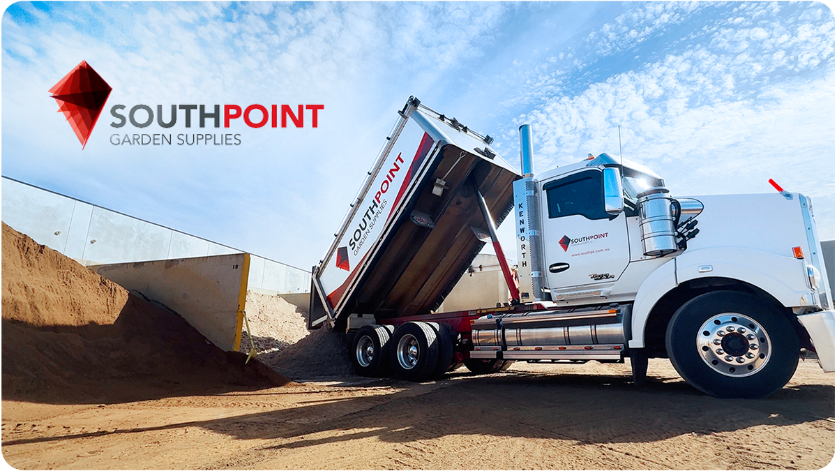A white dump truck with SouthPoint Garden Supplies branding is unloading dirt or sand at a construction or landscaping site, with a blue sky and some clouds in the background.