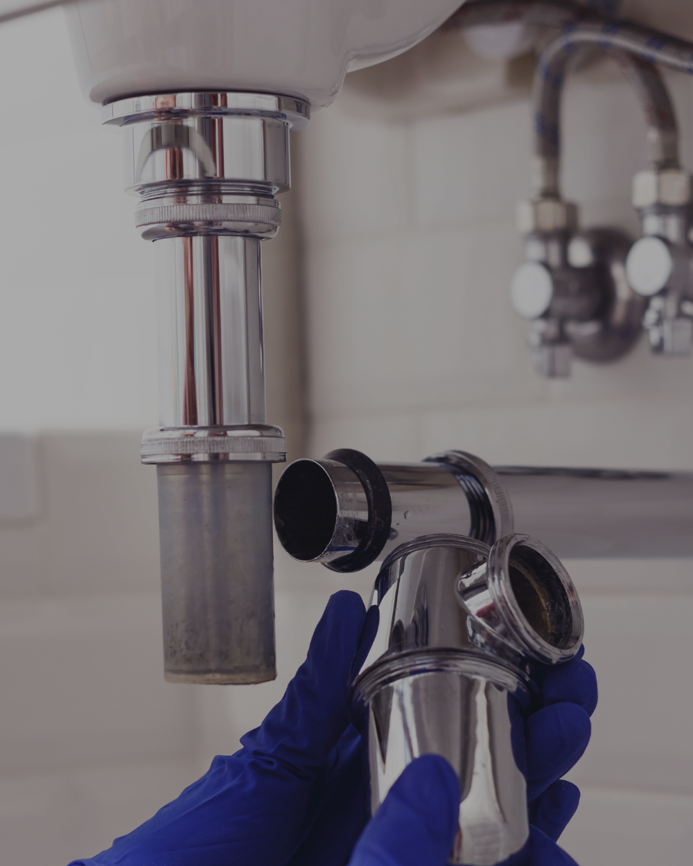 A person wearing blue gloves holding a stainless steel pipe under a sink pipe connection.