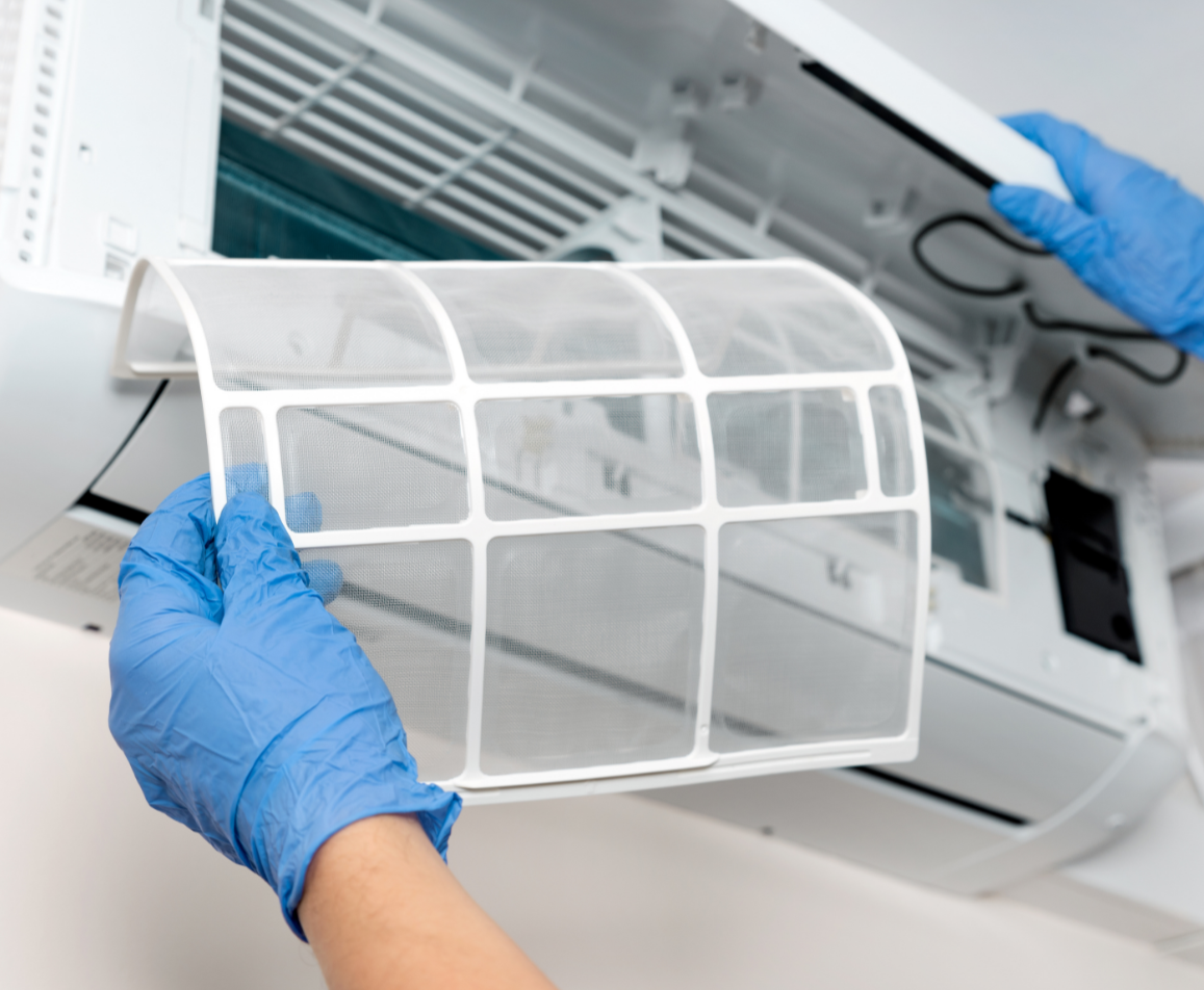 Hand wearing a blue glove removing a lint filter from an air conditioning unit.