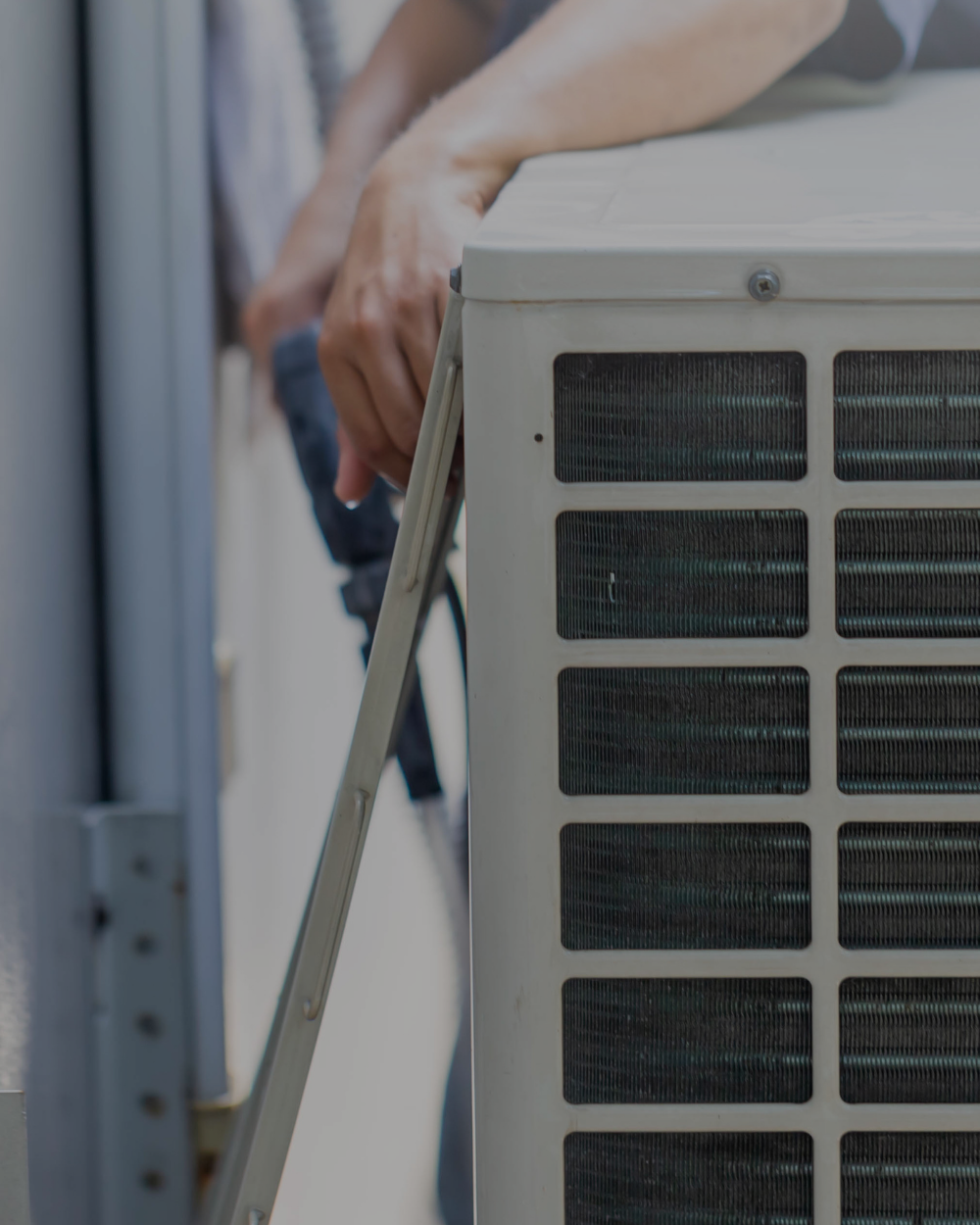 Person performing maintenance on an air conditioning unit, holding a tool and working on the side of the unit.