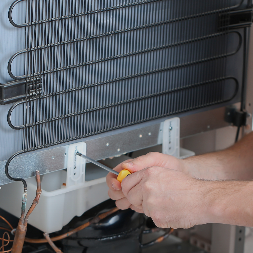 Technician repairing a commercial refrigeration unit and condenser coil