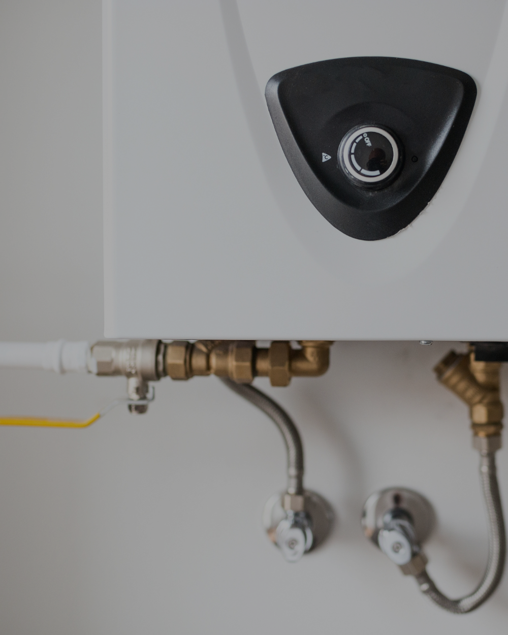 Close-up of a wall-mounted boiler or water heater with a digital control dial, pipes, and valves.