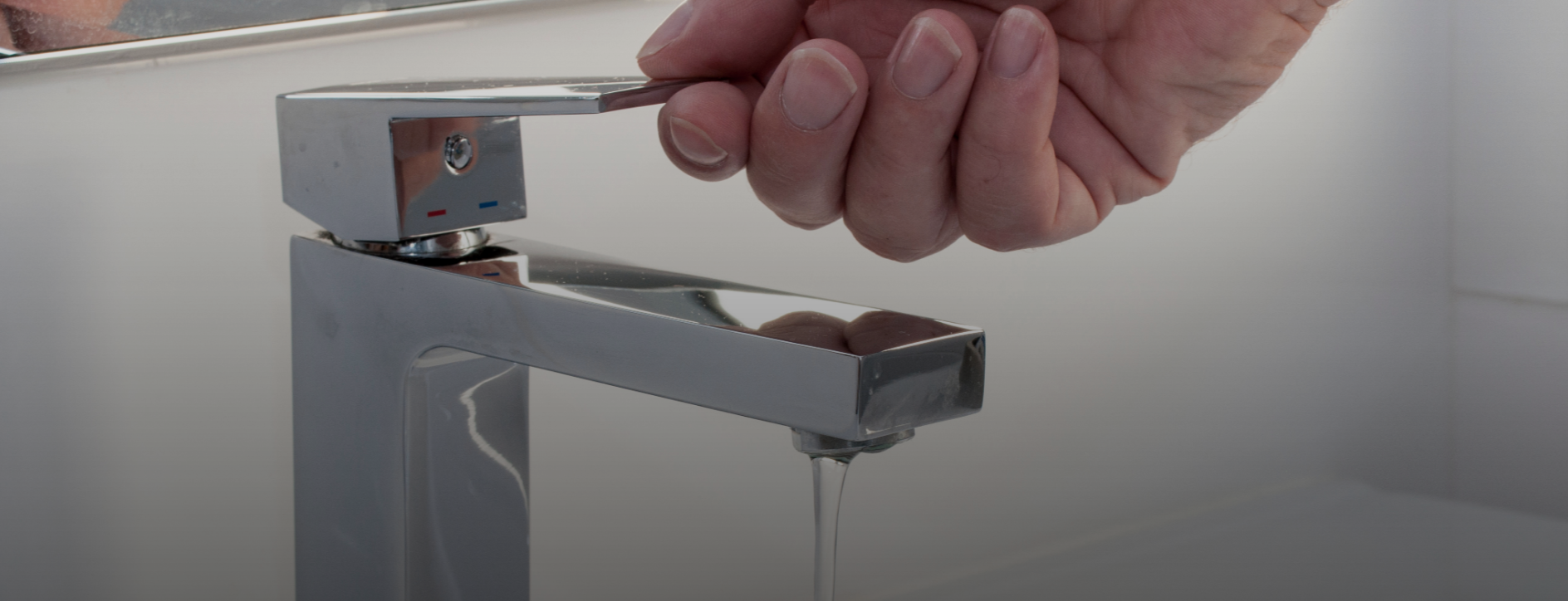 Hand turning on modern bathroom sink faucet with running water