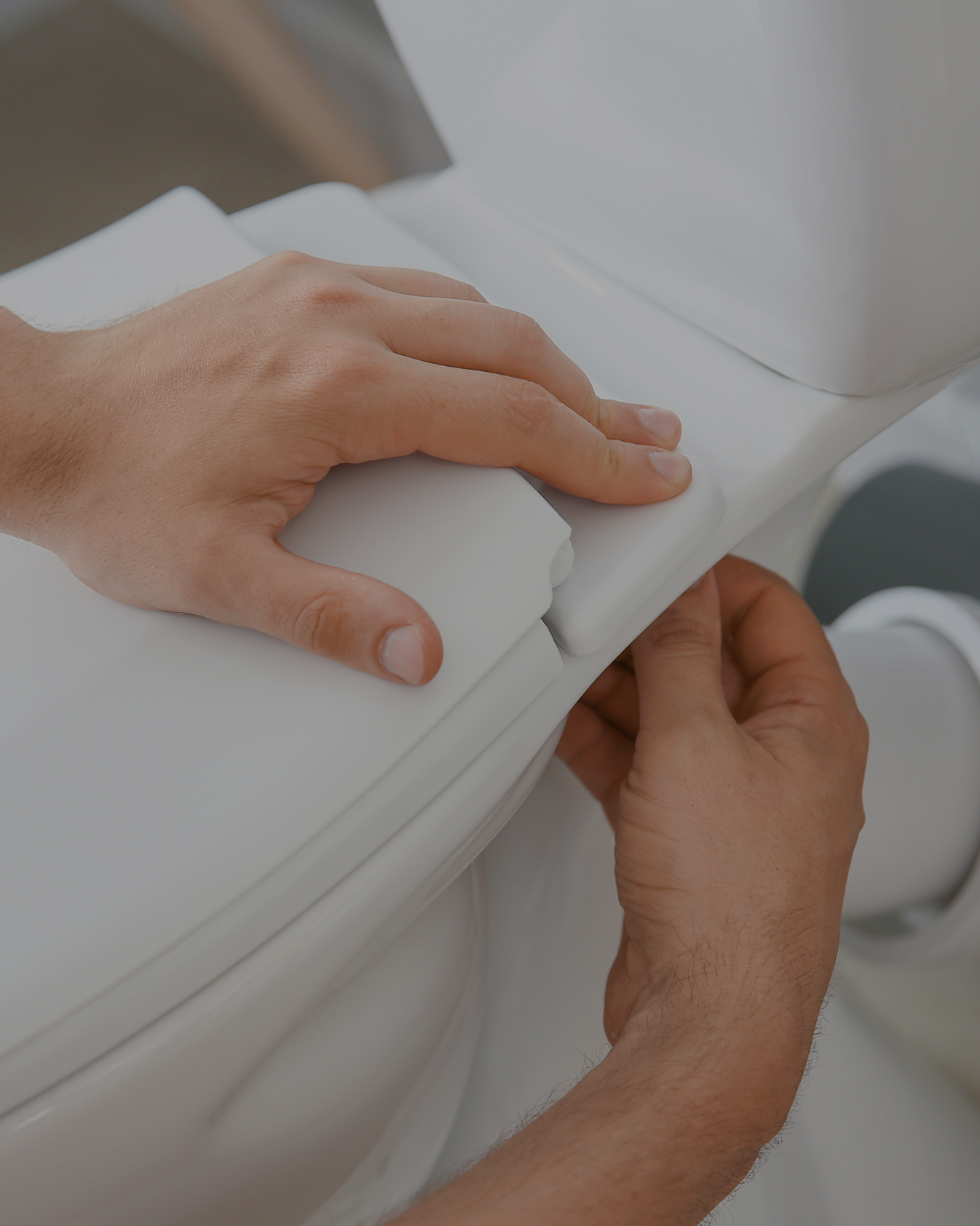 Person adjusting a toilet seat lid in a bathroom.