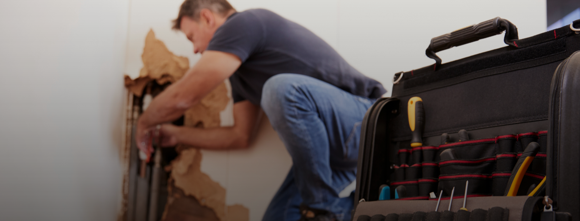 Plumber repairing residential water pipes inside wall with plumbing tools nearby