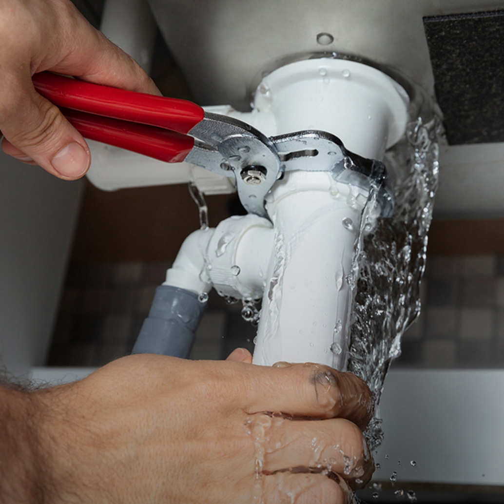 Plumber repairing a leaking drain pipe under a sink during residential plumbing service