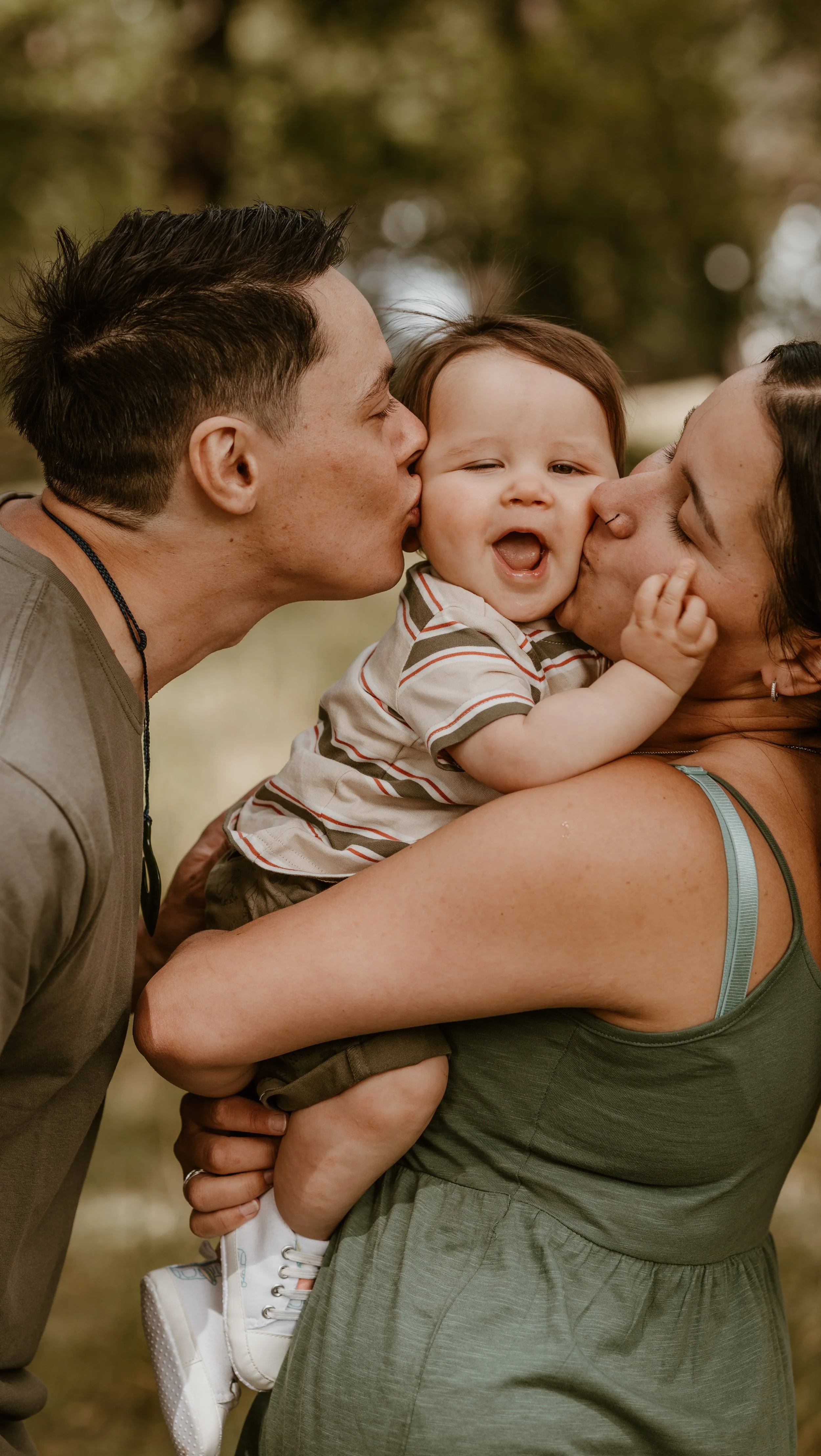 Family of five at the beach, dad and mom kissing, two young boys smiling and one little boy on dad's shoulders