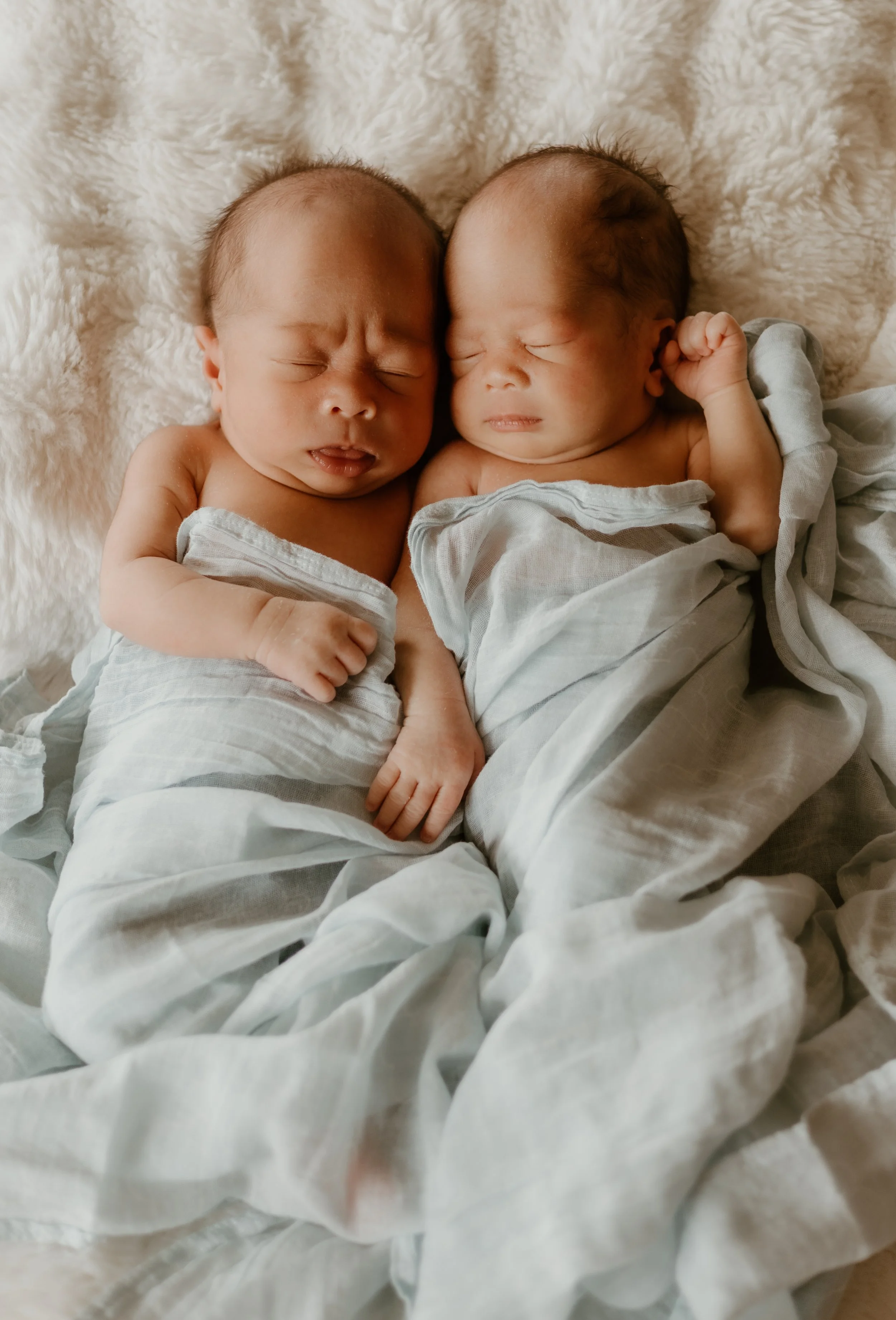 A couple in a field of tall grass during sunset, embracing and looking at each other affectionately.