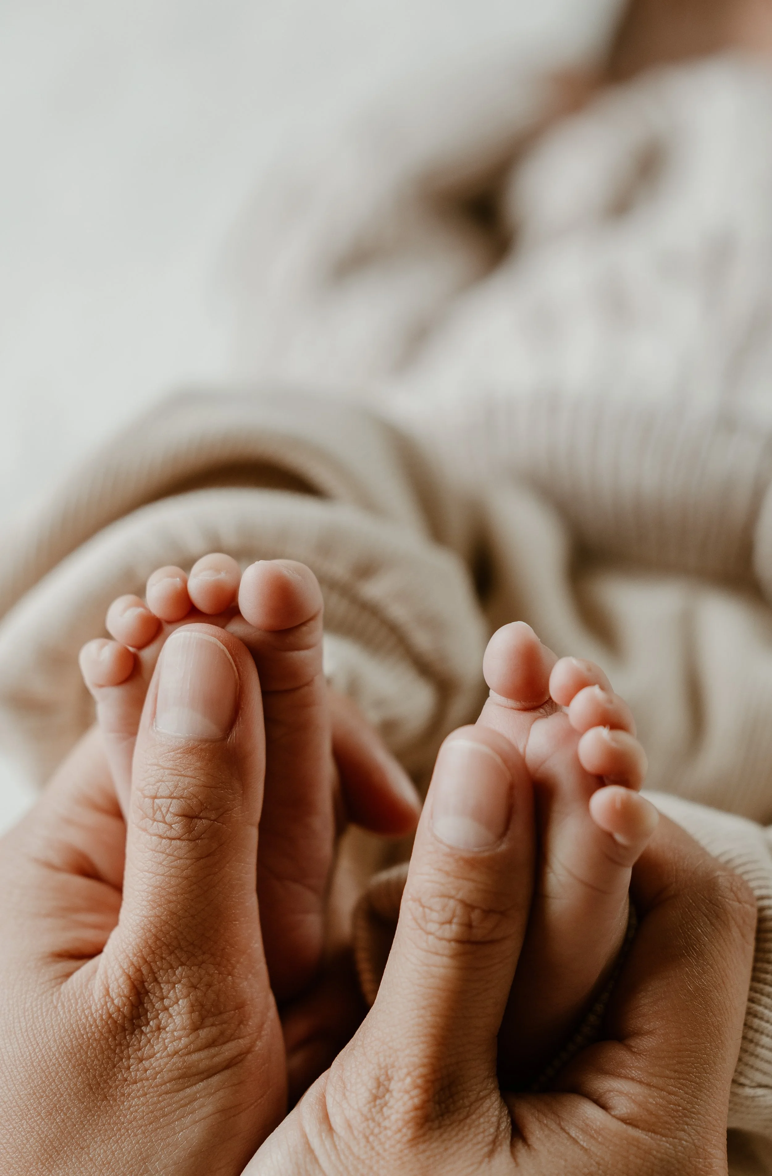 A pregnant woman and a man standing in a grassy field under a cloudy sky, with the woman gently touching her belly and the man looking away.