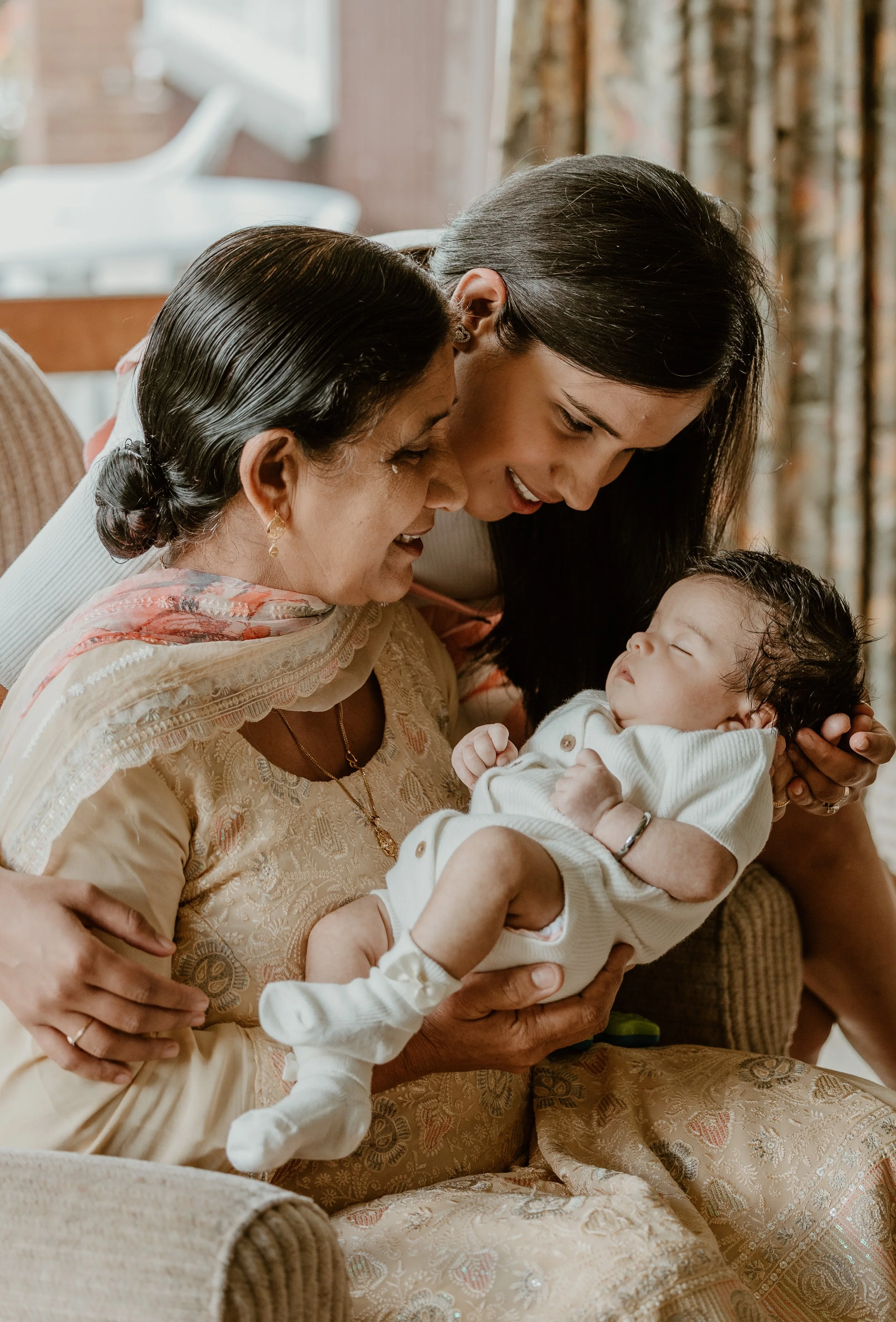 A pregnant woman and a man holding hands walking along a pebble beach during the daytime, with clouds overhead and the ocean in the background.