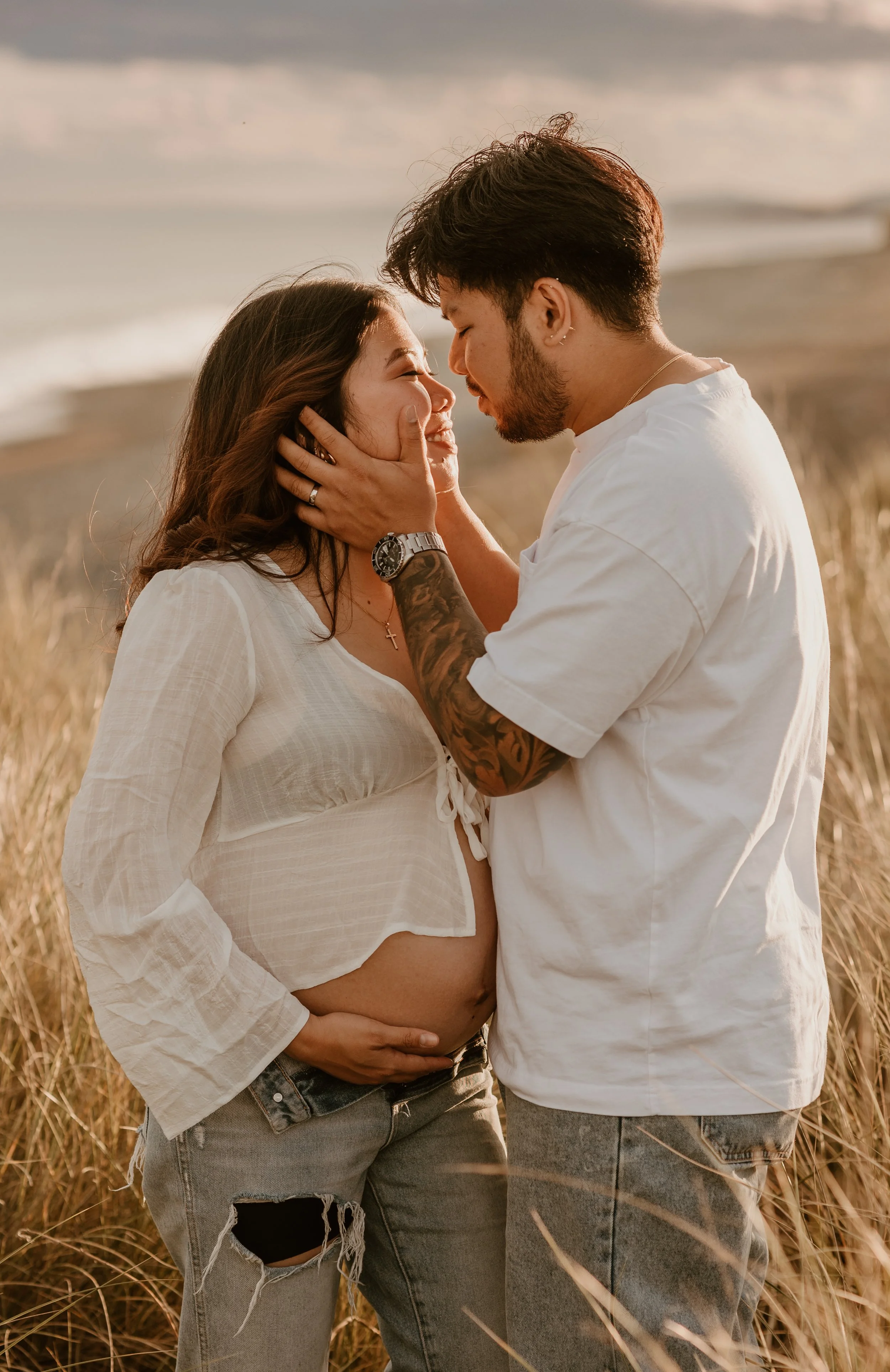 Golden Hour Maternity Glow: Blonde Woman in Burgundy Dress with Blue Eyes Holding Partner’s Arm