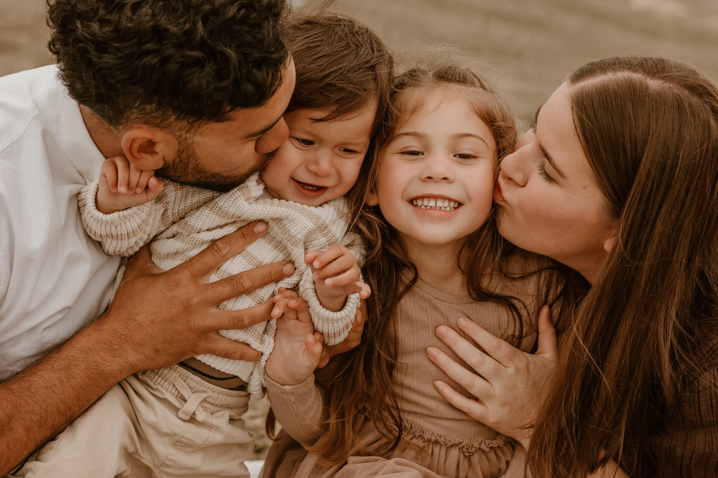 A family of three, a woman, a boy, and a man, sit close together outdoors, laughing and sharing a joyful moment.