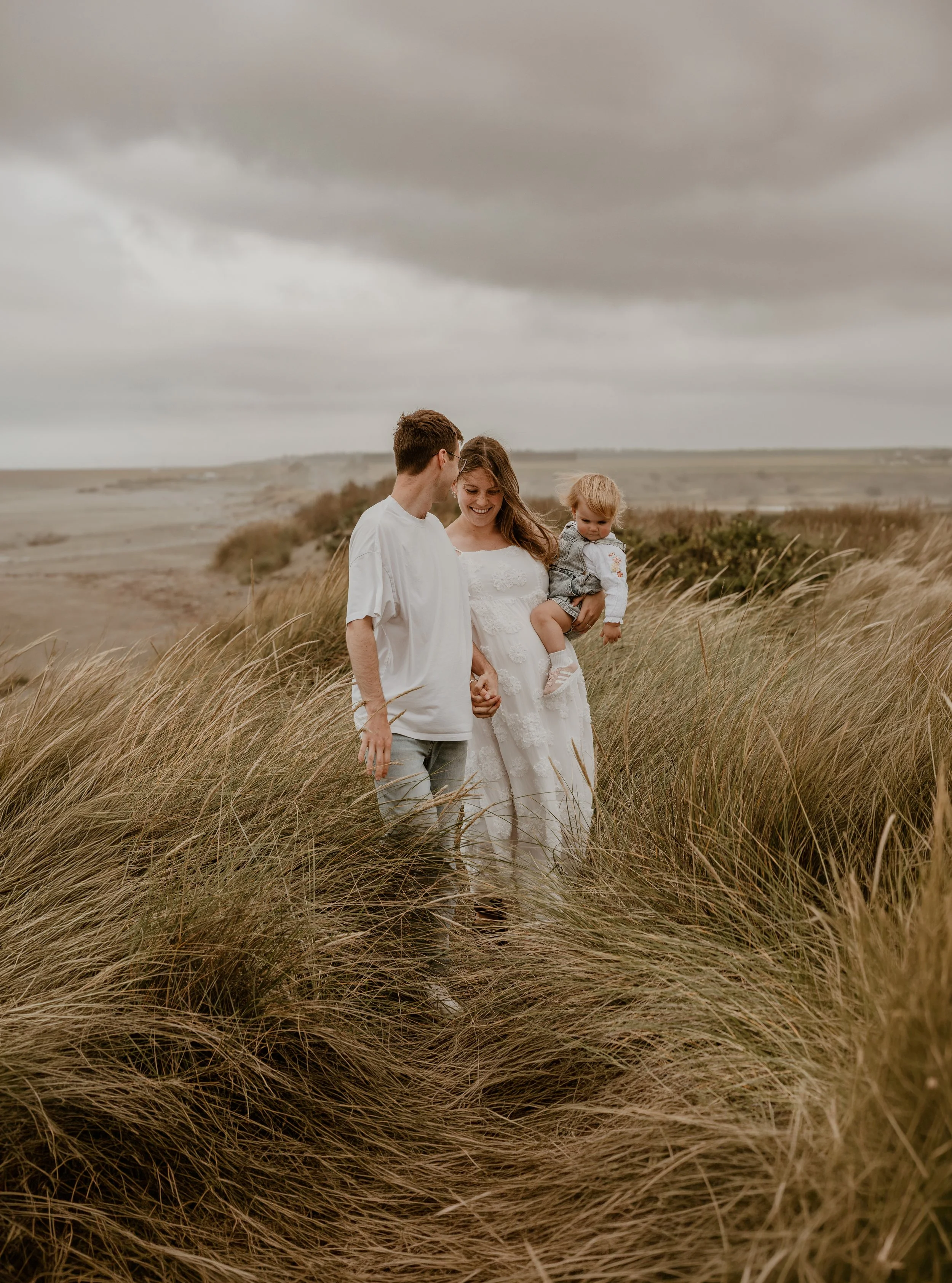 Multiple hands, including children’s, touching a pregnant woman’s belly during a family moment.