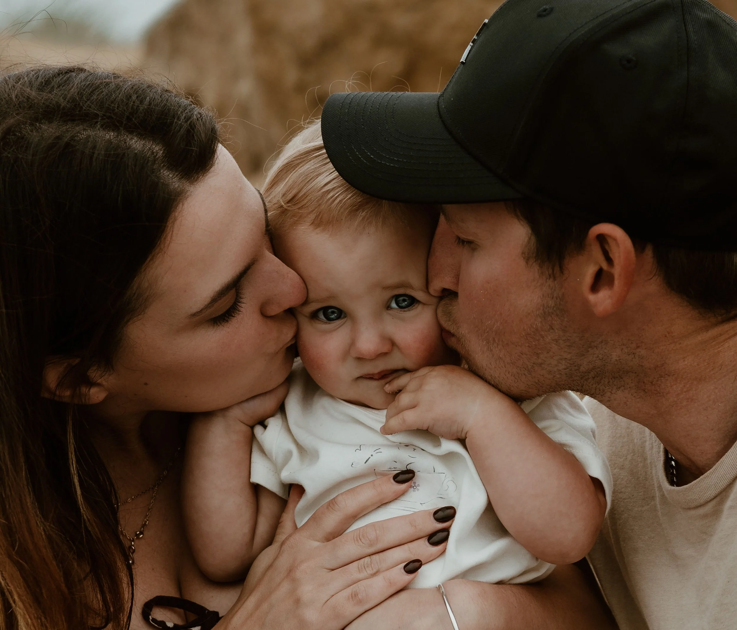 A woman and a man kiss a young child on the cheeks, with the child's face in the center.
