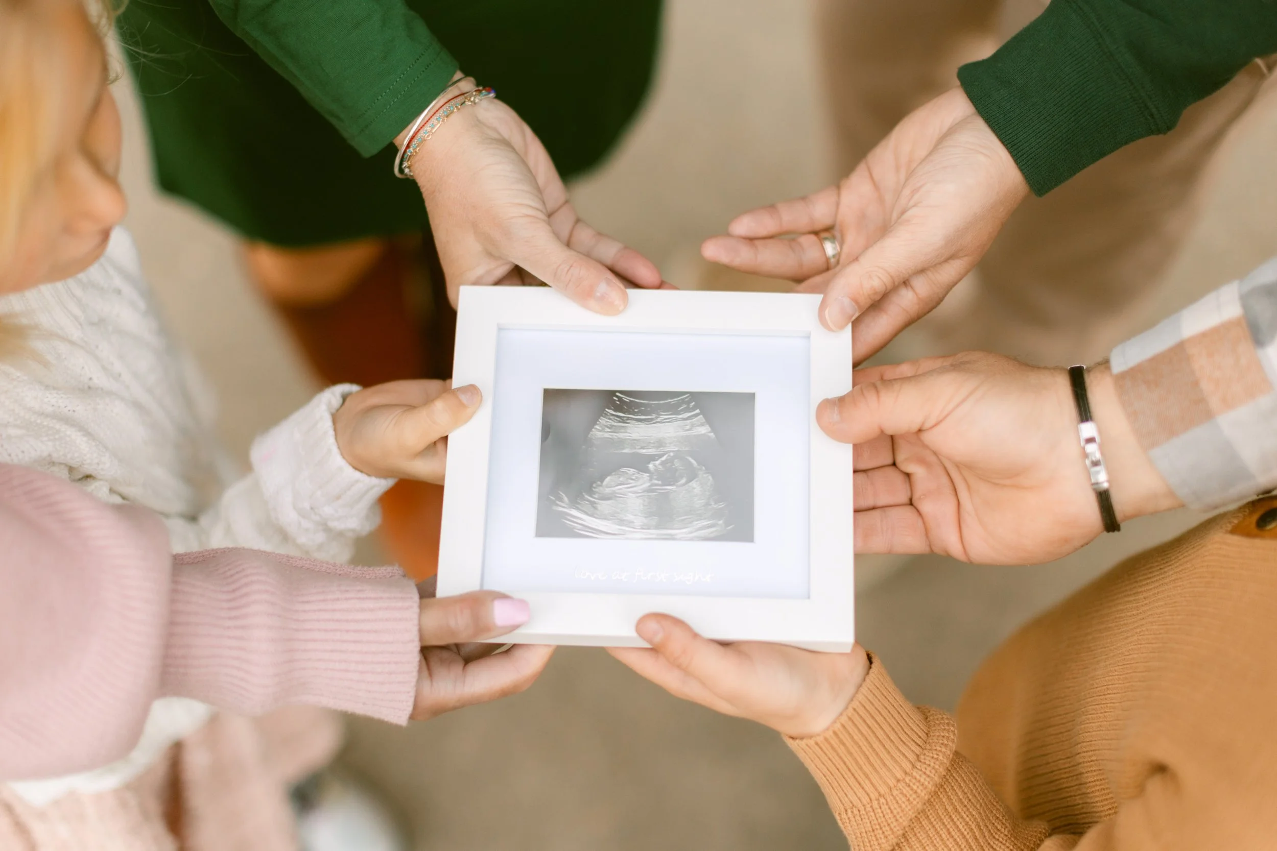 Several people are holding a framed ultrasound photo of a baby, symbolizing pregnancy or upcoming birth.