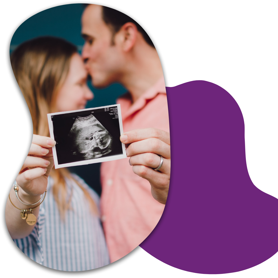 A couple holding an ultrasound image of a fetus, with their foreheads touching and eyes closed, in a close and intimate moment.