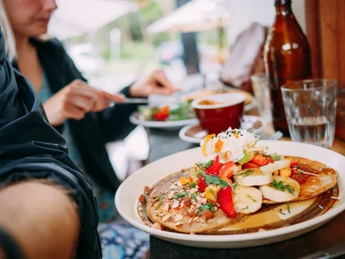 Plate with pancakes topped with strawberries, banana slices, and whipped cream, on a table at a restaurant.
