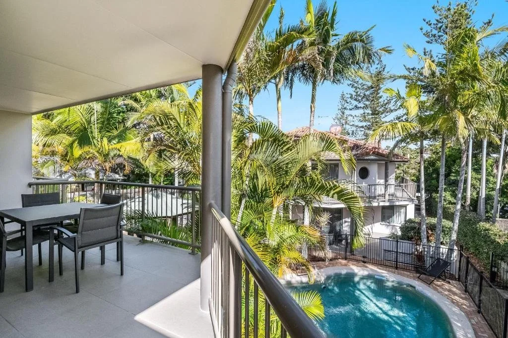 Balcony overlooking a swimming pool surrounded by palm trees at a tropical resort.