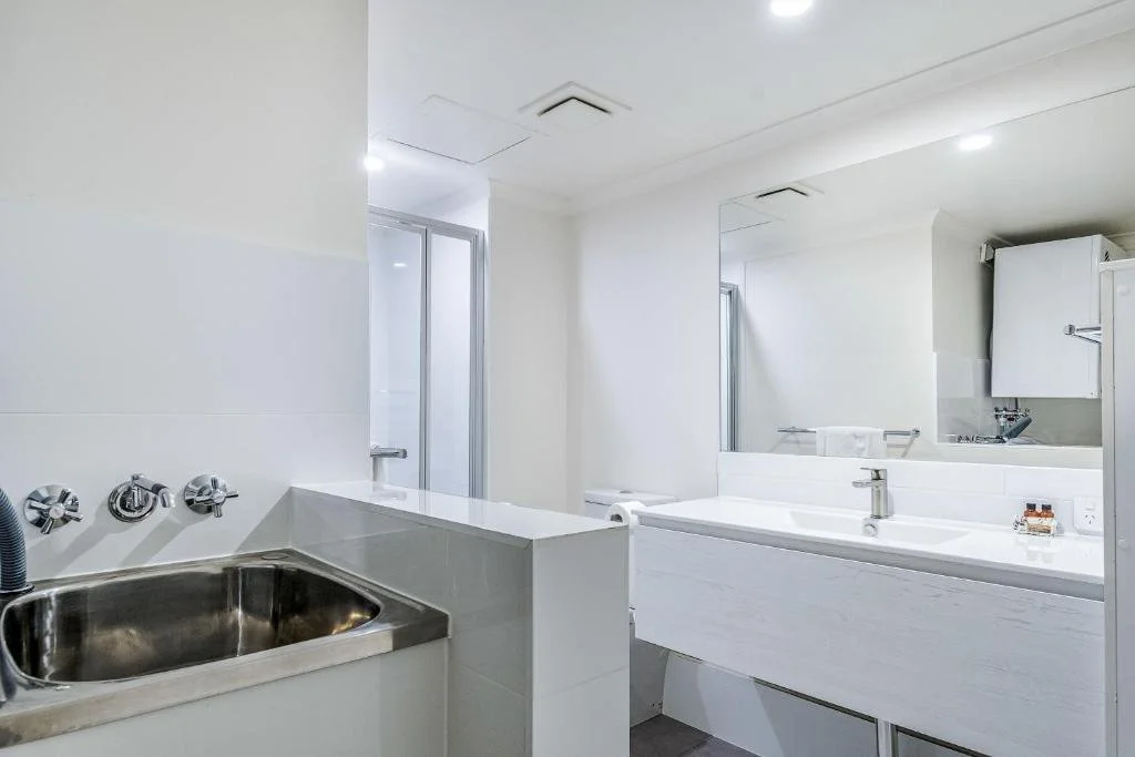 Bathroom with a sink, mirror, and shower area, featuring white walls and modern fixtures.