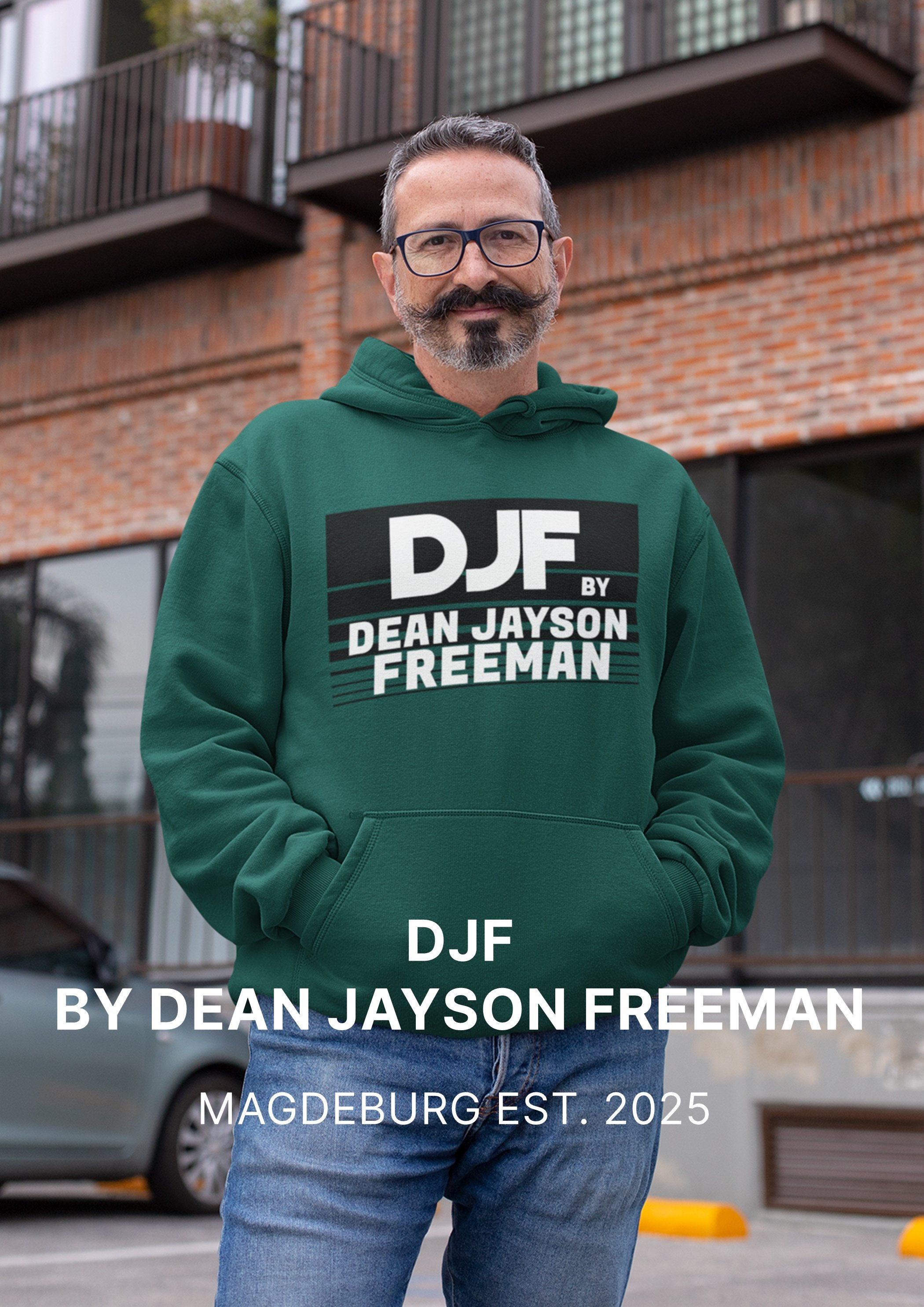Ein Mann trägt eine grüne Kapuzenjacke mit einem Druck, der den Text 'DJF by Dean Jayson Freeman' zeigt, vor einem modernen Backsteingebäude in einer Stadt.