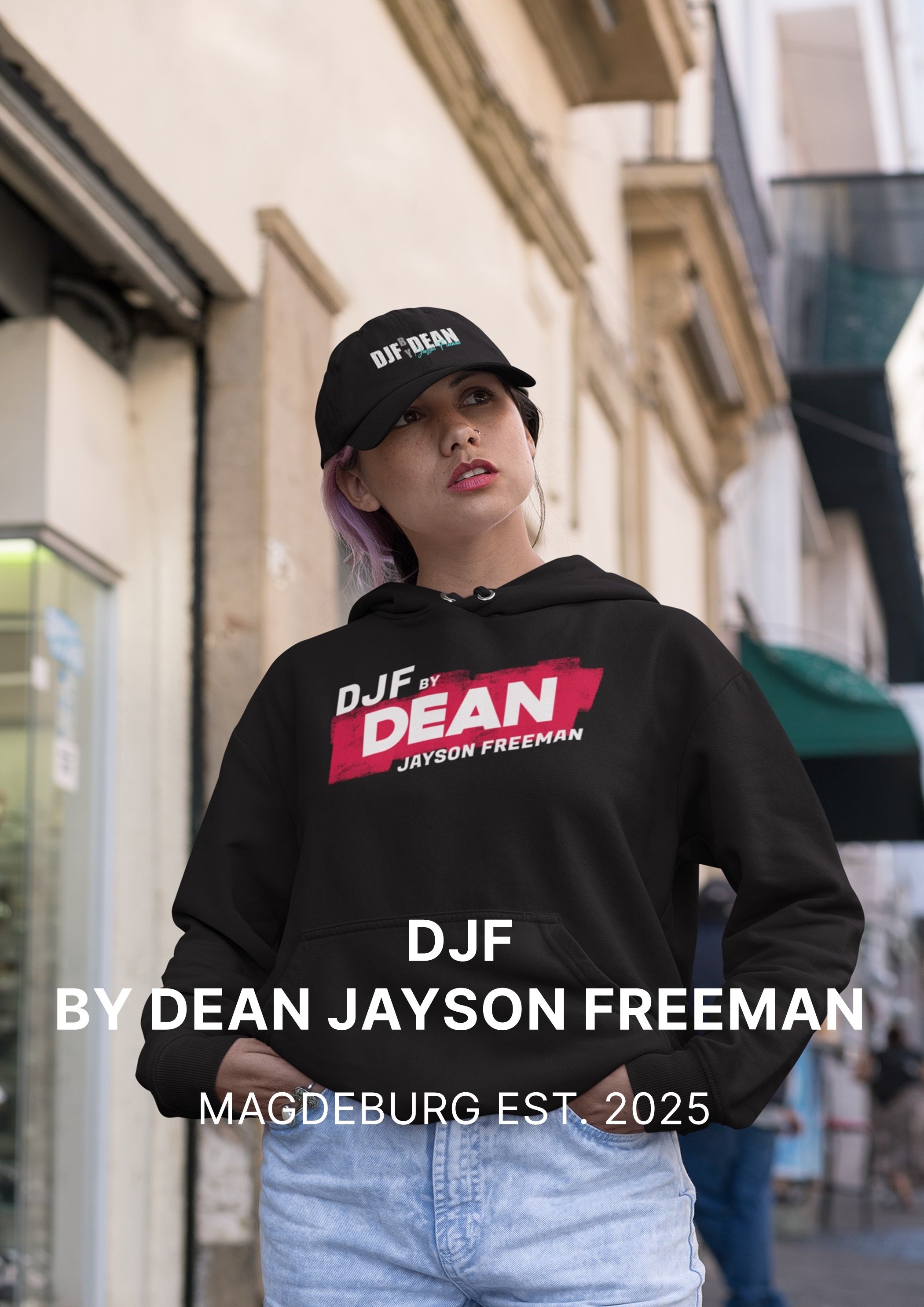 Junge Frau in schwarzen Hoodie mit 'DJF by Dean Jayson Freeman' Logo und schwarzer Cap, stehend in der Stadt, Blick nach oben, kurze Haare mit lila Farbhighlights.