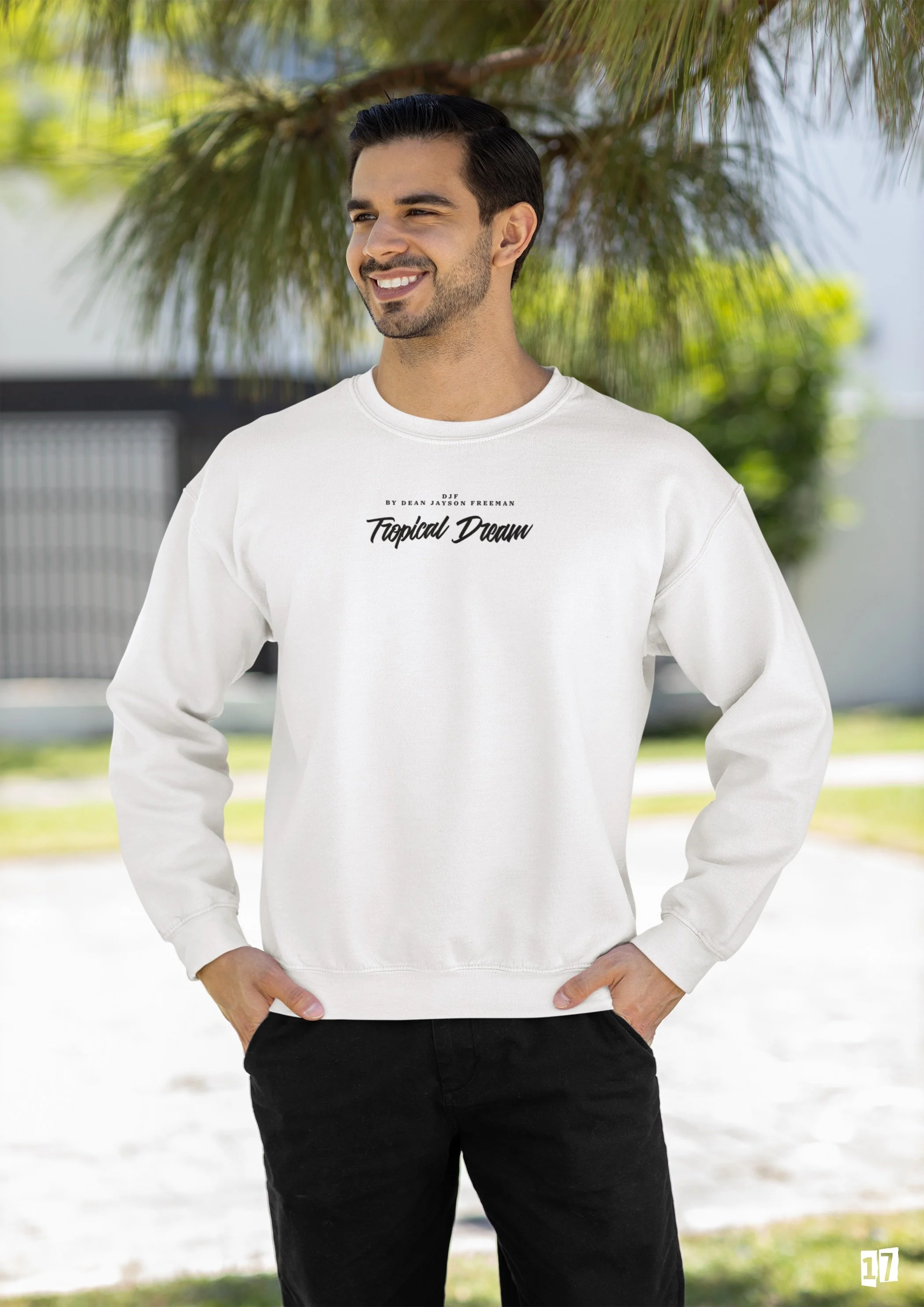 Junge Mann trägt weißen Pullover mit Text 'Tropical Dream' auf einem sonnigen Tag im Freien, umgeben von Palmen