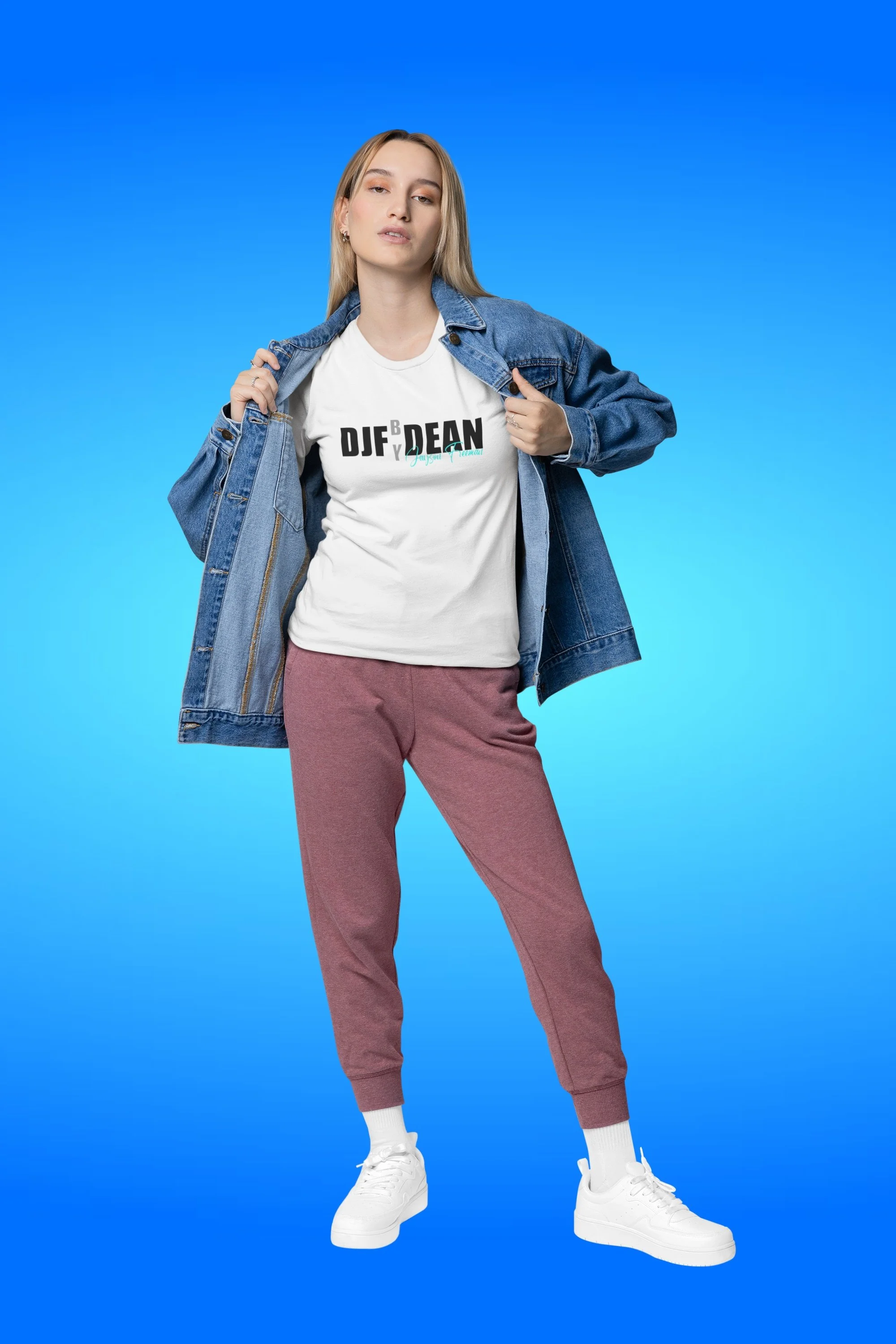 Junge Frau in bequemen Sportkleidung, trage weißes T-Shirt mit schwarzem und türkisem Text, blaue Jeansjacke, maroon Jogginghose, weiße Sportschuhe, steht vor blauem Hintergrund.