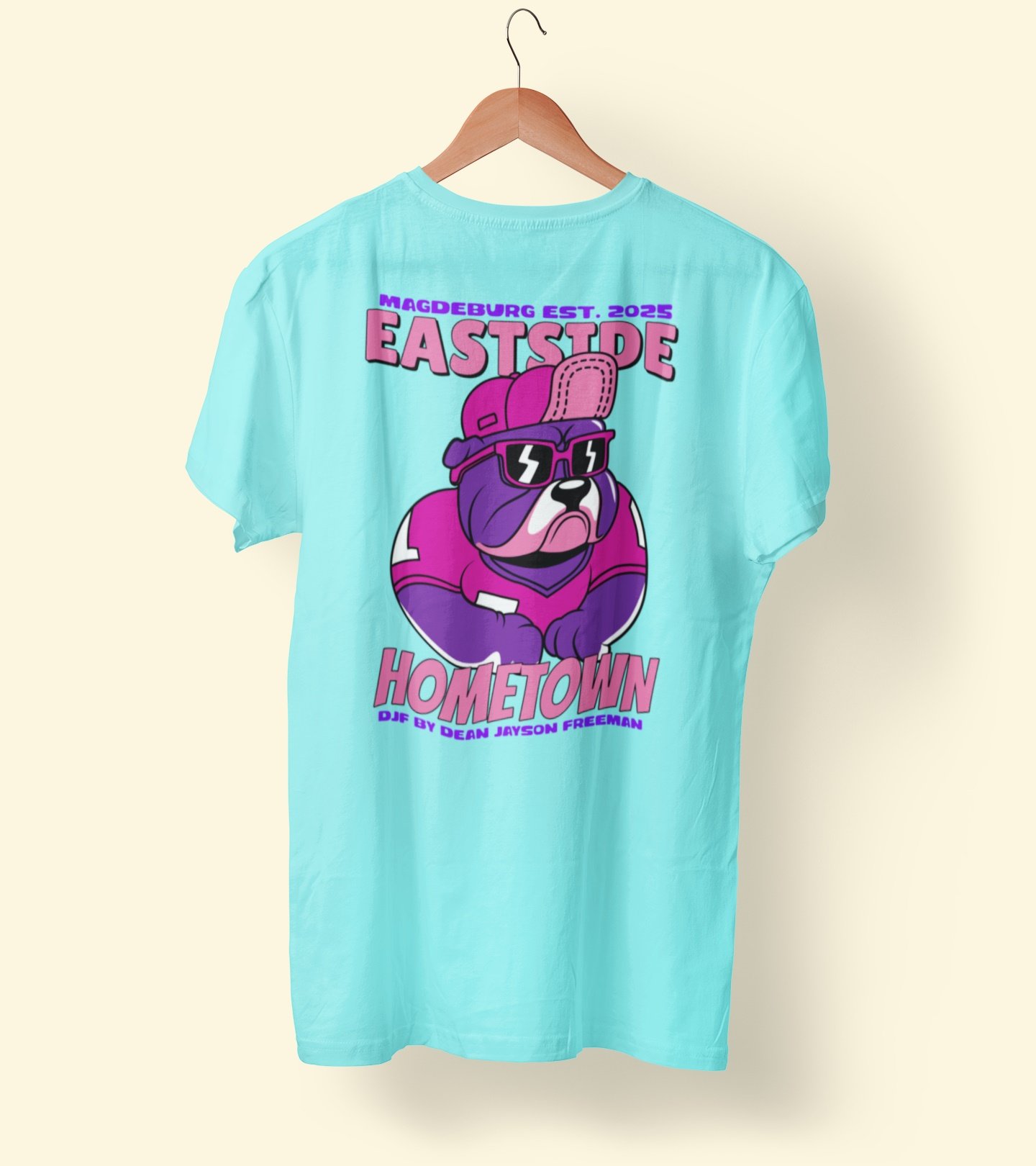Hellblaues T-Shirt mit grafischem Druck eines Hundes mit Sonnenbrille und Rucksack, Text 'Magdeburg Est. 2025', 'Eastside Hometown', und DJ by Dean Jayson Freeman.