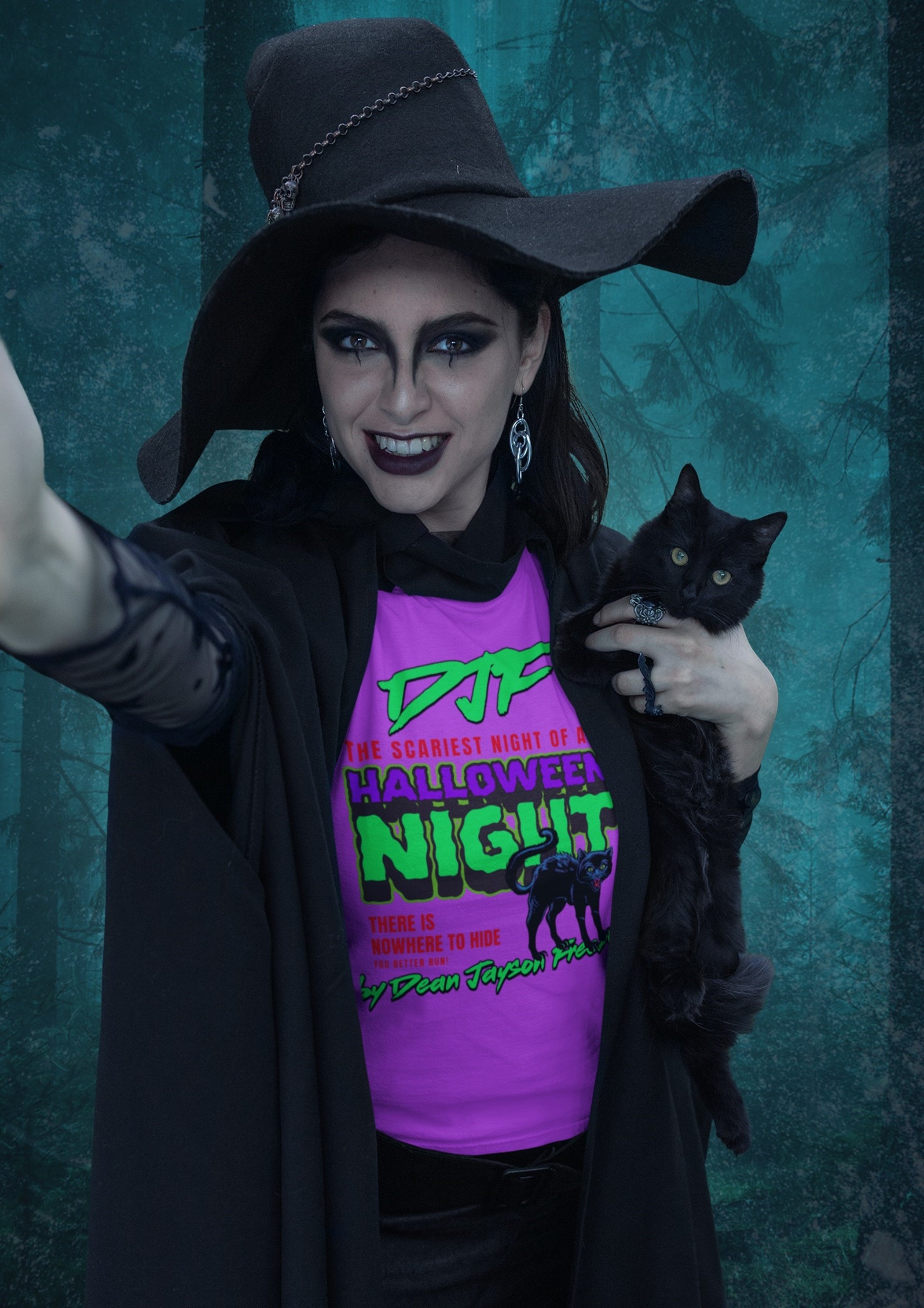 Eine Frau trägt einen schwarzen Hexenhut mit Kettenverzierung, dunklem Make-up und einem schwarzen Kleid. Sie hält eine schwarze Katze mit grünen Augen und einem silbernen Halsband. Im Hintergrund ein dunkler Wald mit Bäumen.