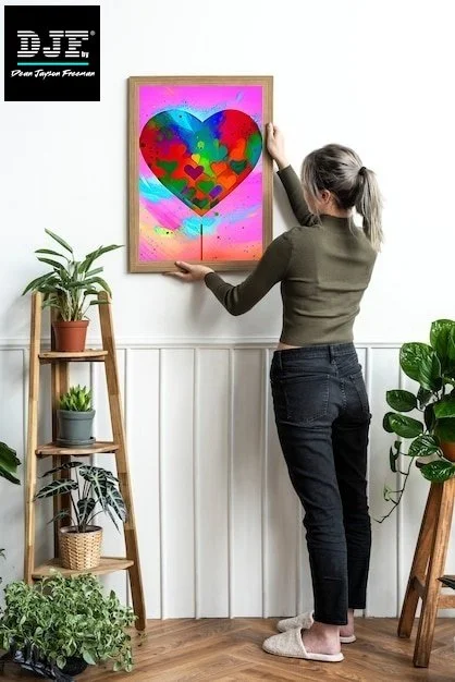 Frau hängt ein buntes Herzbild in einem Bilderrahmen an die Wand in einem Raum mit Pflanzen.