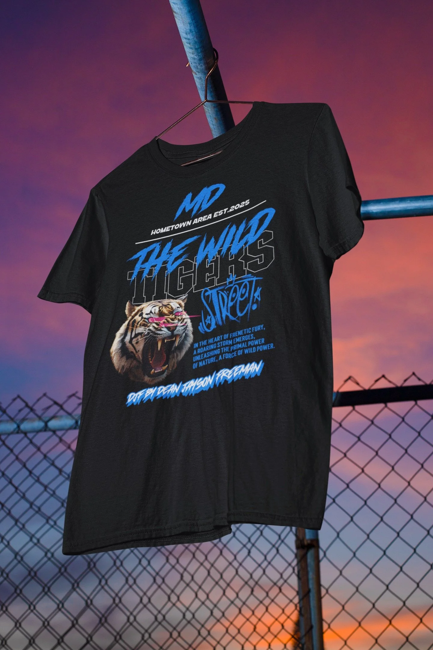 Schwarzes T-Shirt mit bunt bedrucktem Design, hängt an einem Metalldraht, im Hintergrund ein Sonnenuntergang