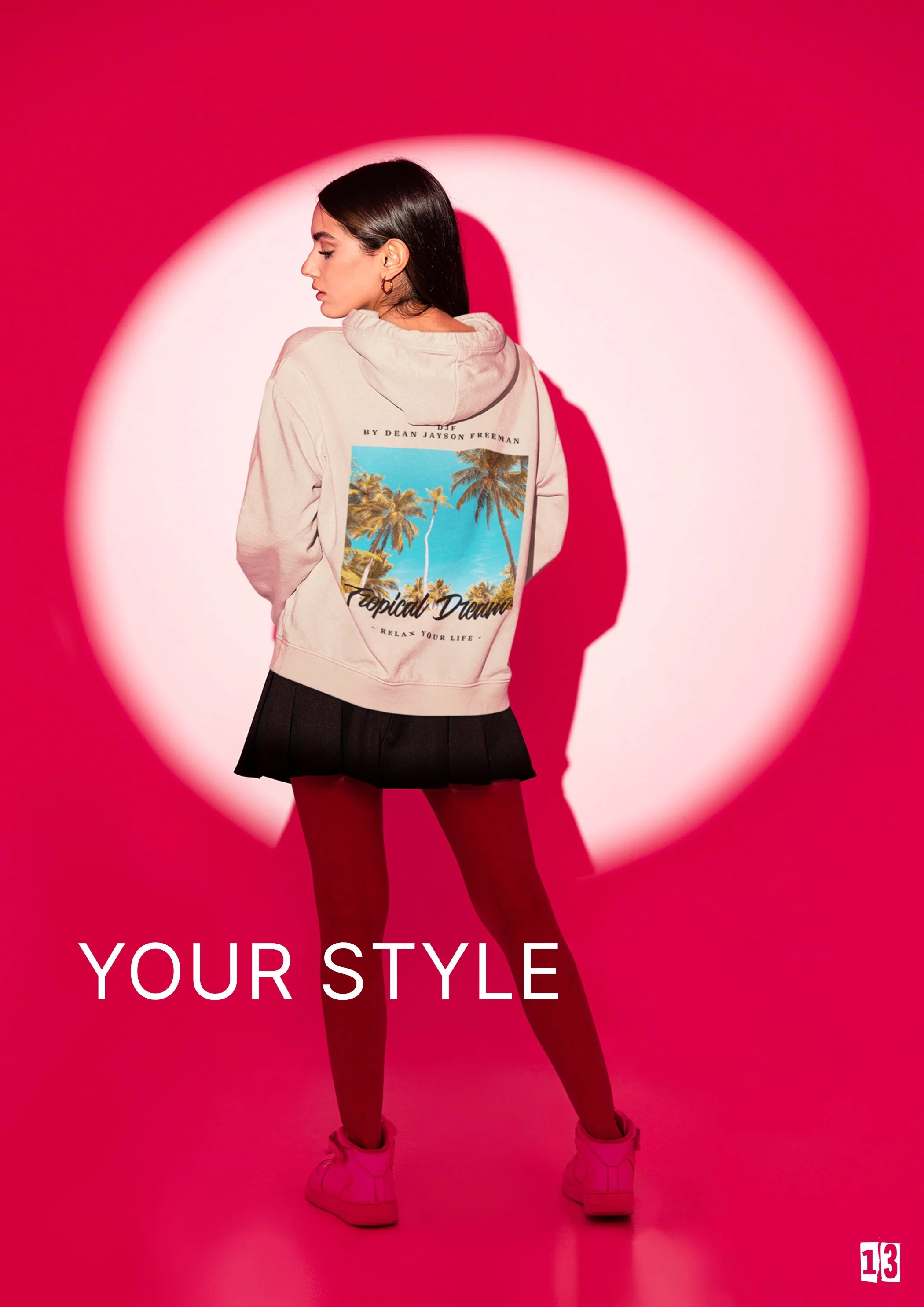 Eine junge Frau steht vor einem pinkfarbenen Hintergrund mit einem weißen Lichtring. Sie trägt eine beige Kapuzenjacke mit einem tropischen Palmen-Print auf der Rückseite, einer schwarzen Miniskirt, rote Strümpfe und weiße Turnschuhe. Der Text auf de