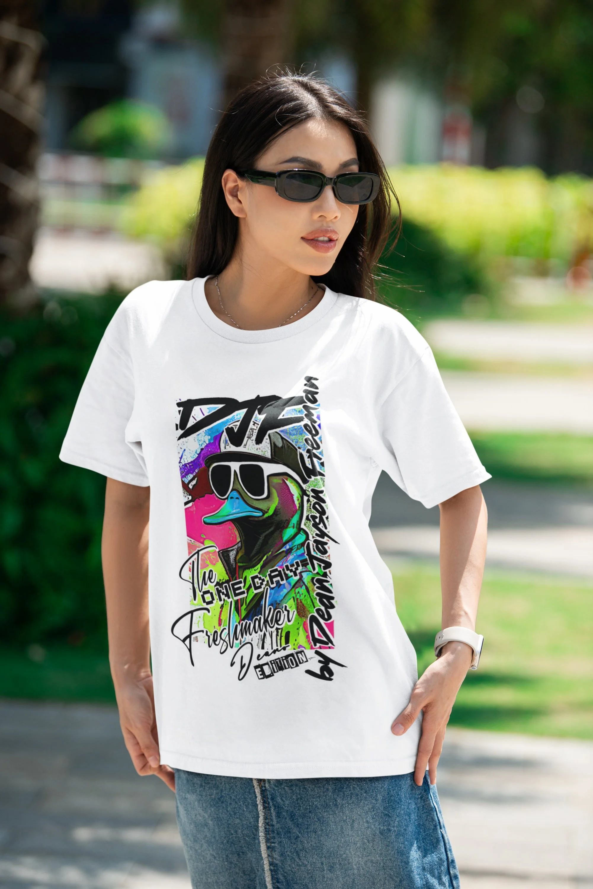 Junge Frau trägt T-Shirt mit buntem Mode-Design, Sonnenbrille und Armbanduhr, steht im Freien in sonnigem Park.