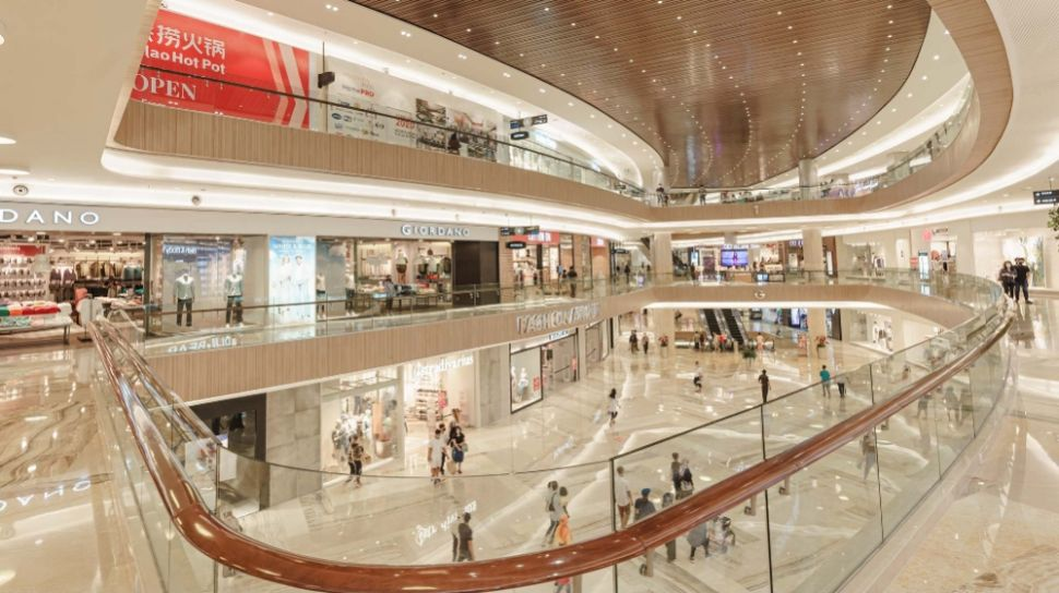 Multiple levels of a modern shopping mall with shops, glass railings, and shoppers walking on the floors.