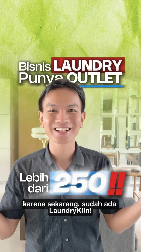 A smiling man in a gray shirt standing indoors with a sign promoting Laundry Punya Outlet, mentioning it has over 250 LaundryKlin services.