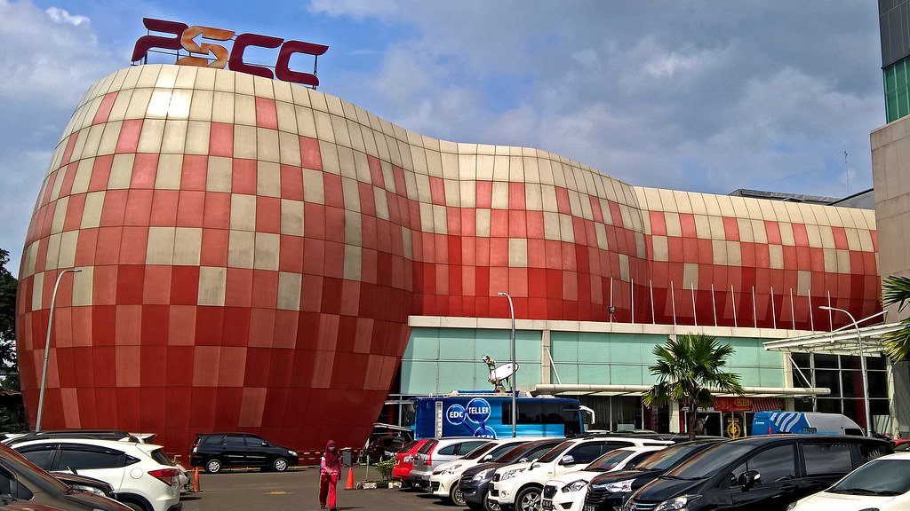 A large building with a curved, checkered red and beige exterior, housing the EDC (Economic Development Corporation) logo on top, with a parking lot filled with cars in front.