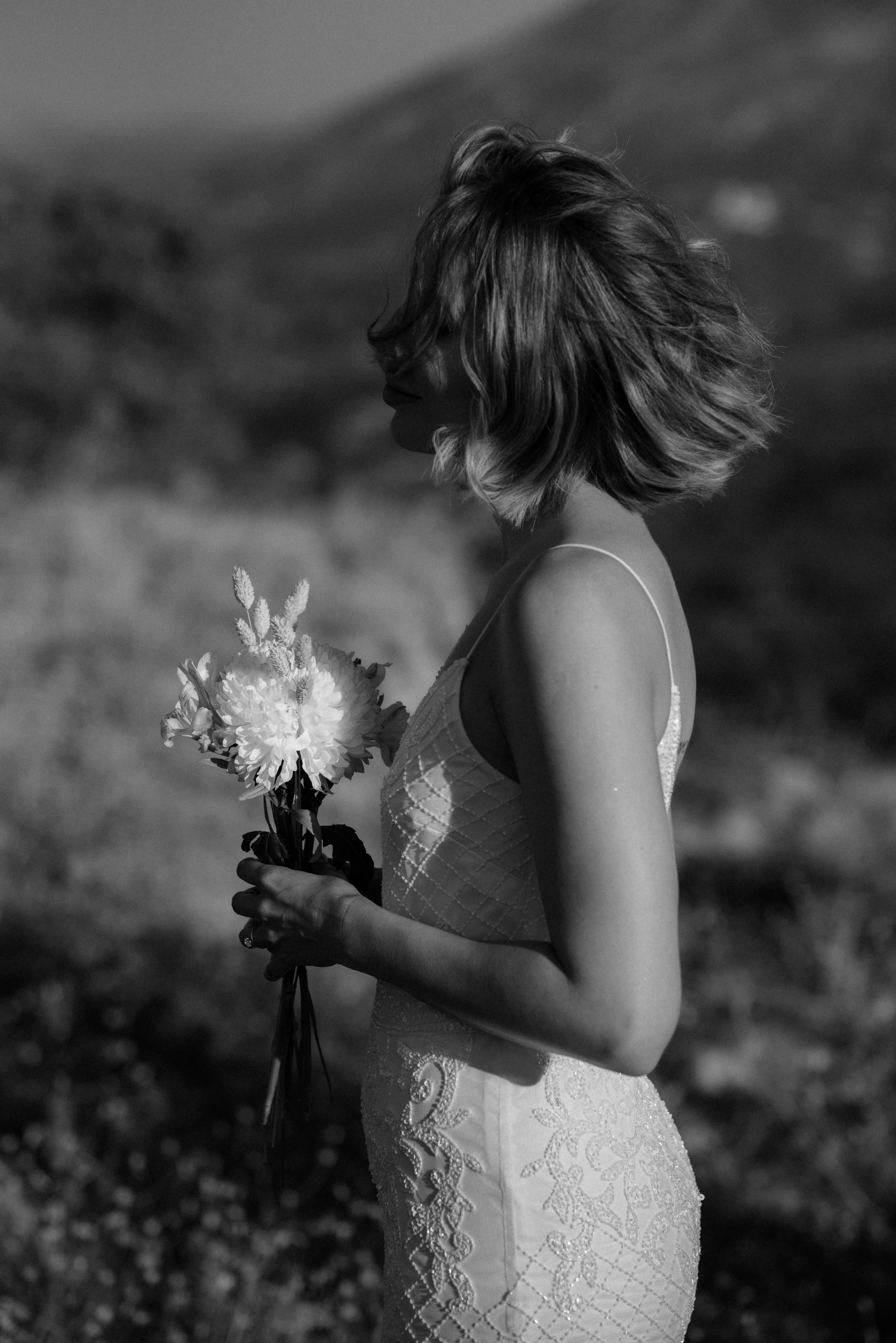 A woman with short hair holding a bouquet of flowers, standing outdoors on a sunny day.