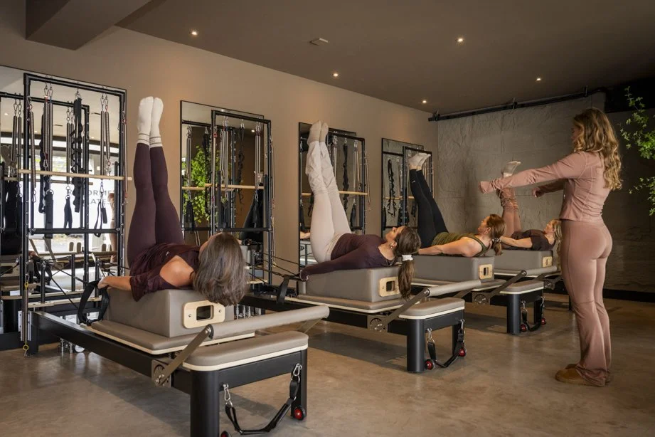 Vier vrouwen krijgen Pilates-lessen onder begeleiding van een instructeur in een fitnessstudio.