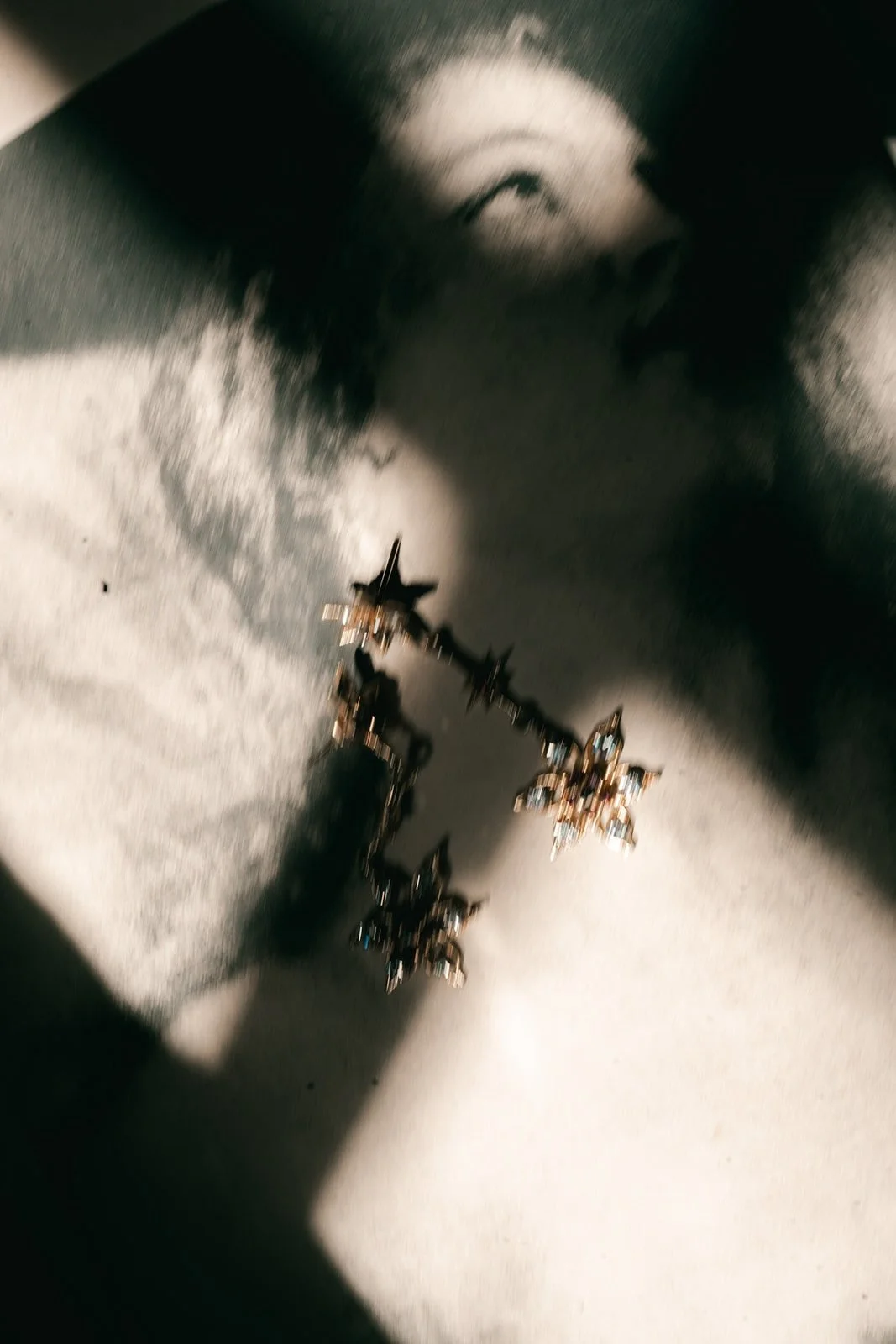 A person’s face with eyes closed and mouth open, with sunlight casting shadows. The person is wearing a star-shaped earring with multiple pointed tips that appears to have small gemstones.