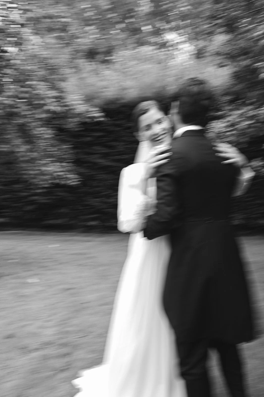 A black and white photo of a bride and groom dancing outdoors, with motion blur.