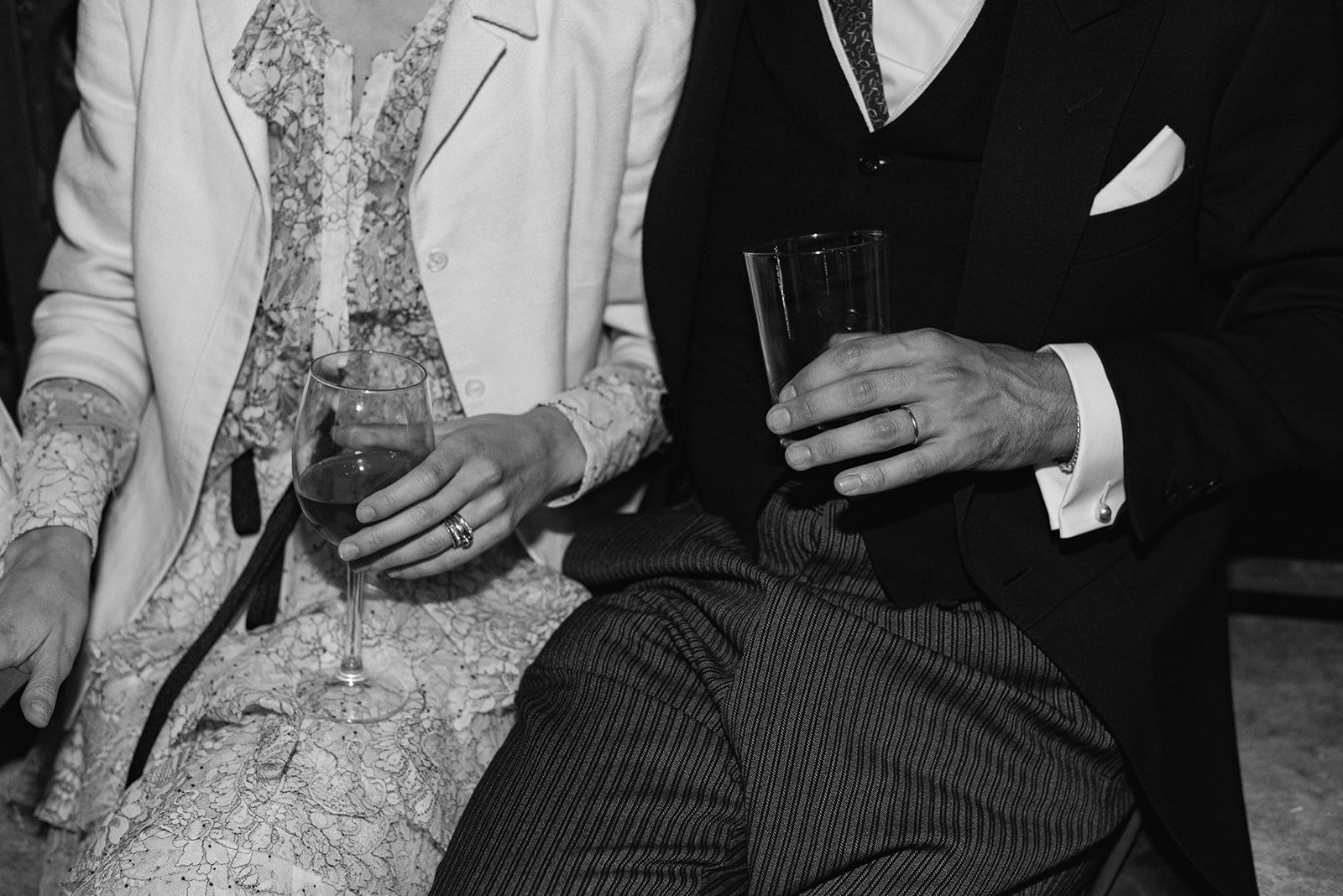 Close-up of a man and woman sitting together, holding glasses of wine at a social event, black and white.