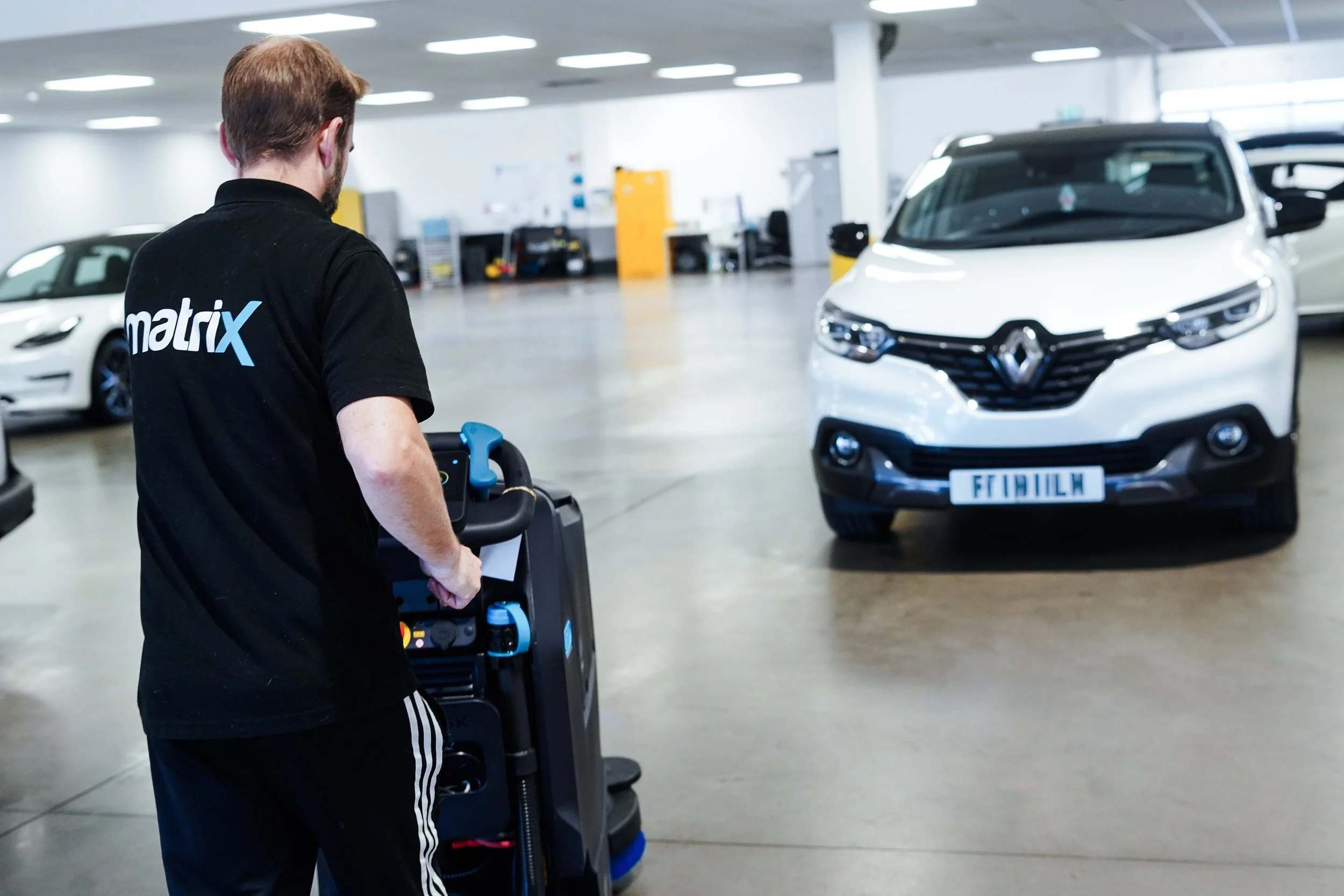 A person cleaning a white Renault car in an indoor parking garage.