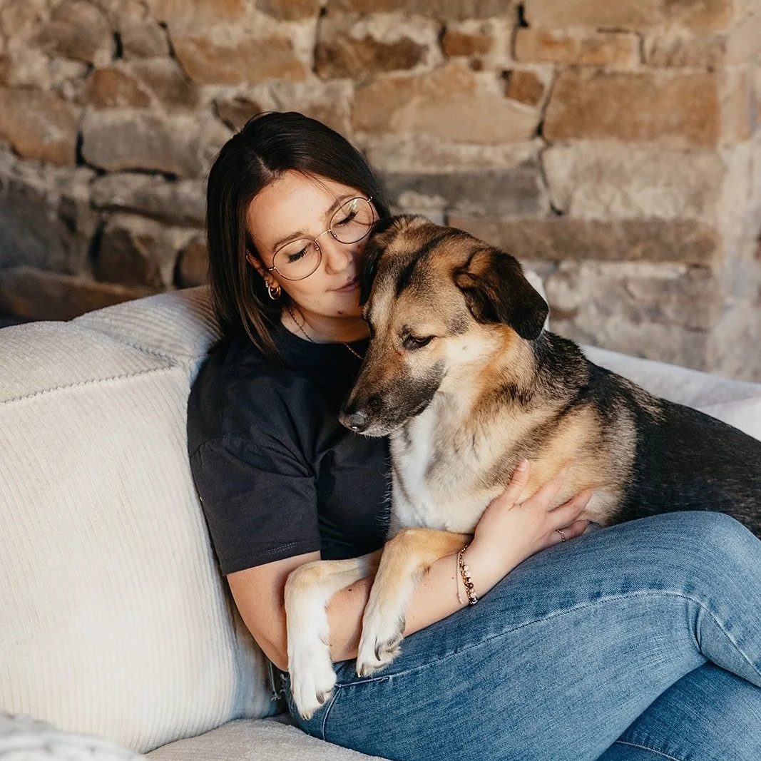 Eine Frau sitzt auf einer Couch, hält einen Hund im Arm und kuschelt mit ihm, vor einer Steilsteinwand.