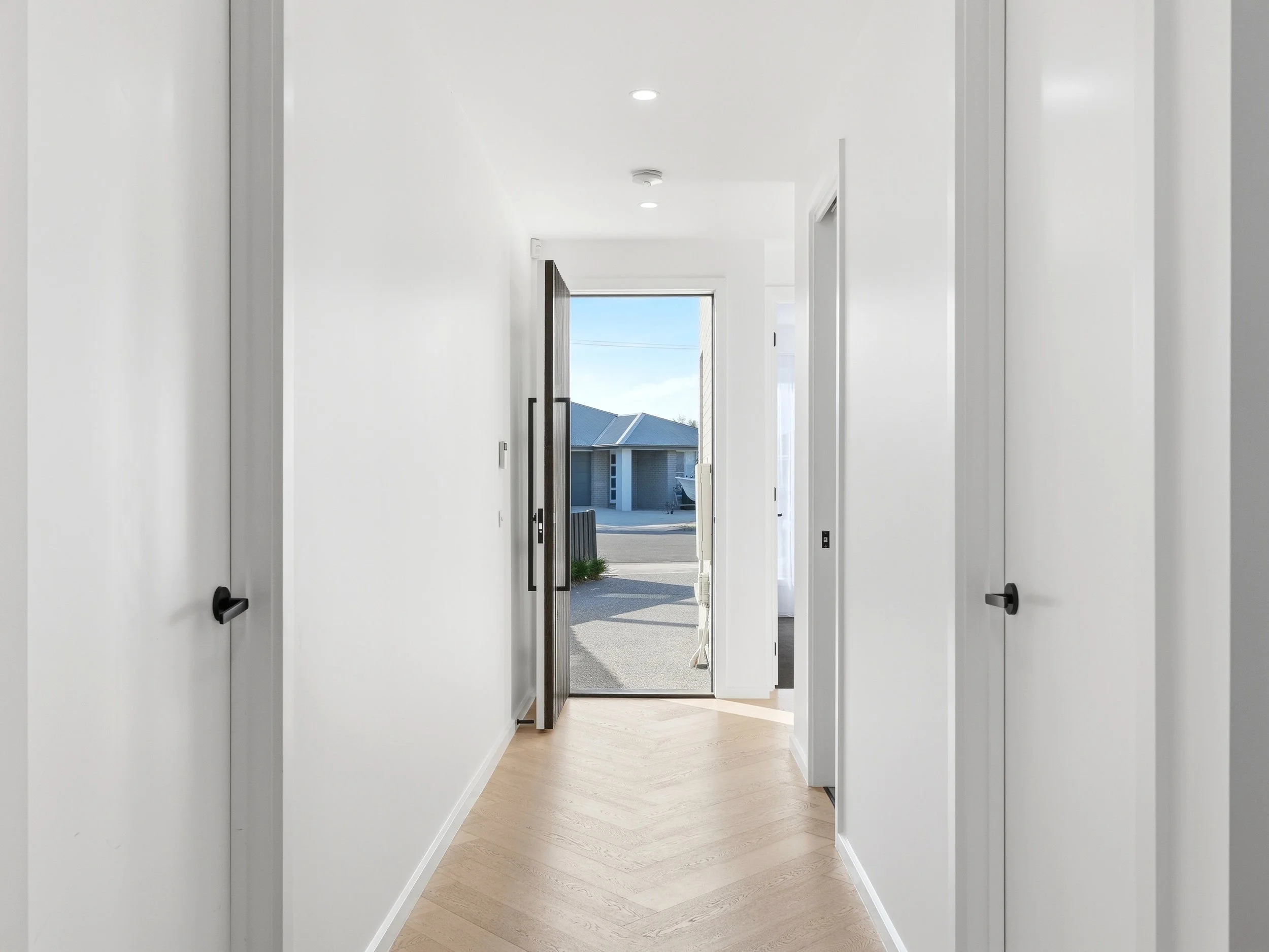 A bright, modern interior hallway leading to an open front door with a view of a residential neighborhood outside.