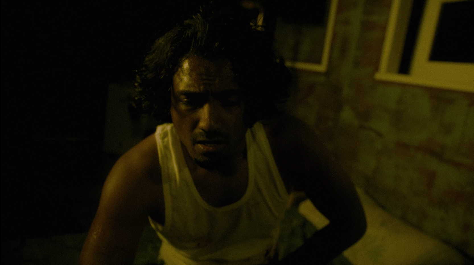 A person in a yellow tank top looking up at the camera in a dark room.