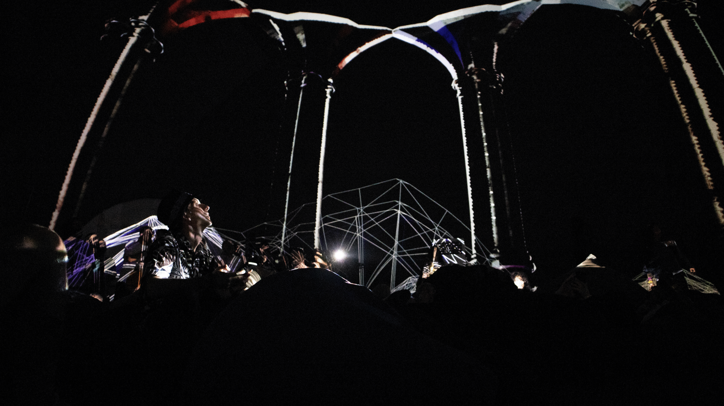 Nighttime outdoor concert with performers on stage and geometric light projections.